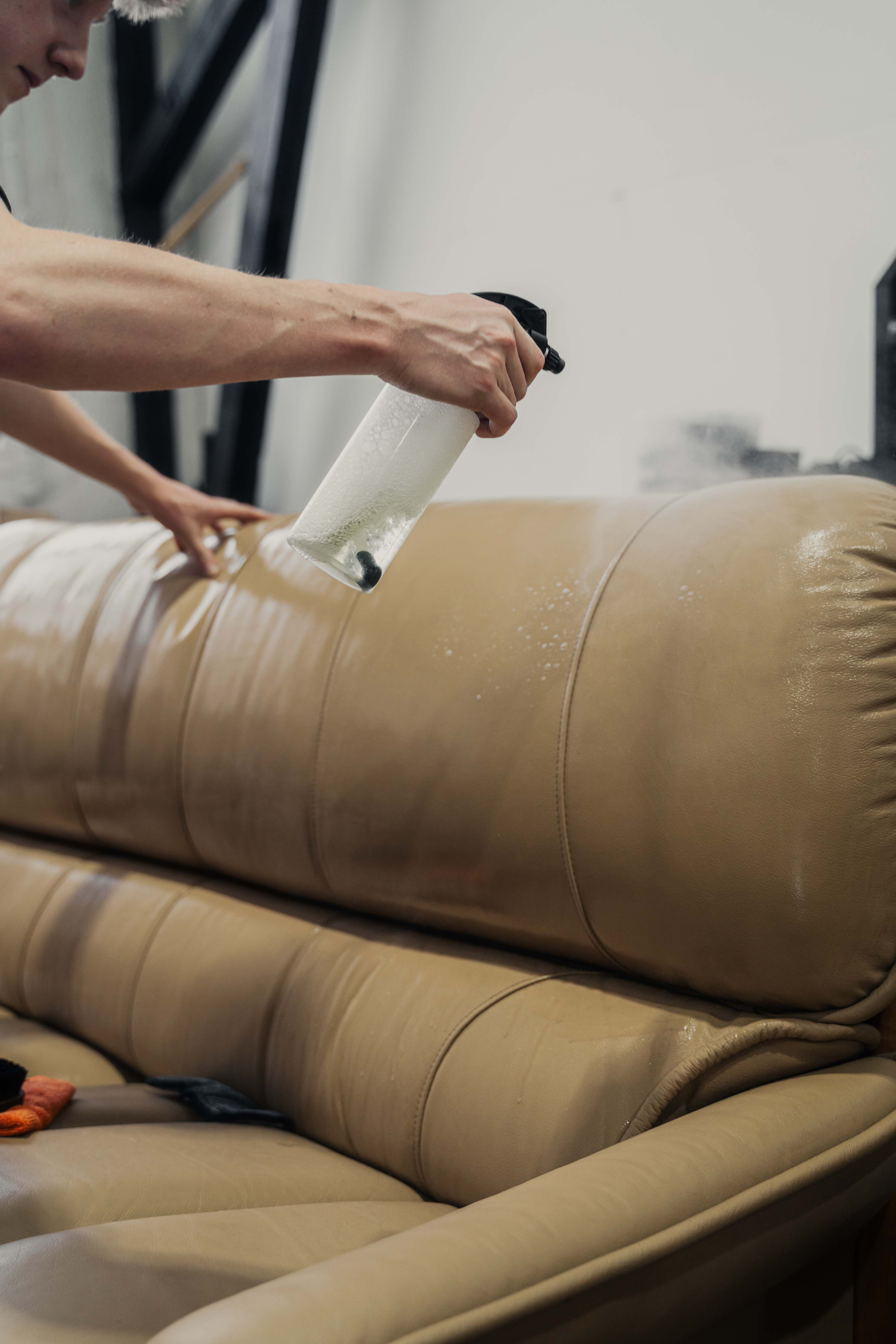 Canberra Leather technician spraying Geist leather cleaner onto a tan leather sofa — Canberra ACT