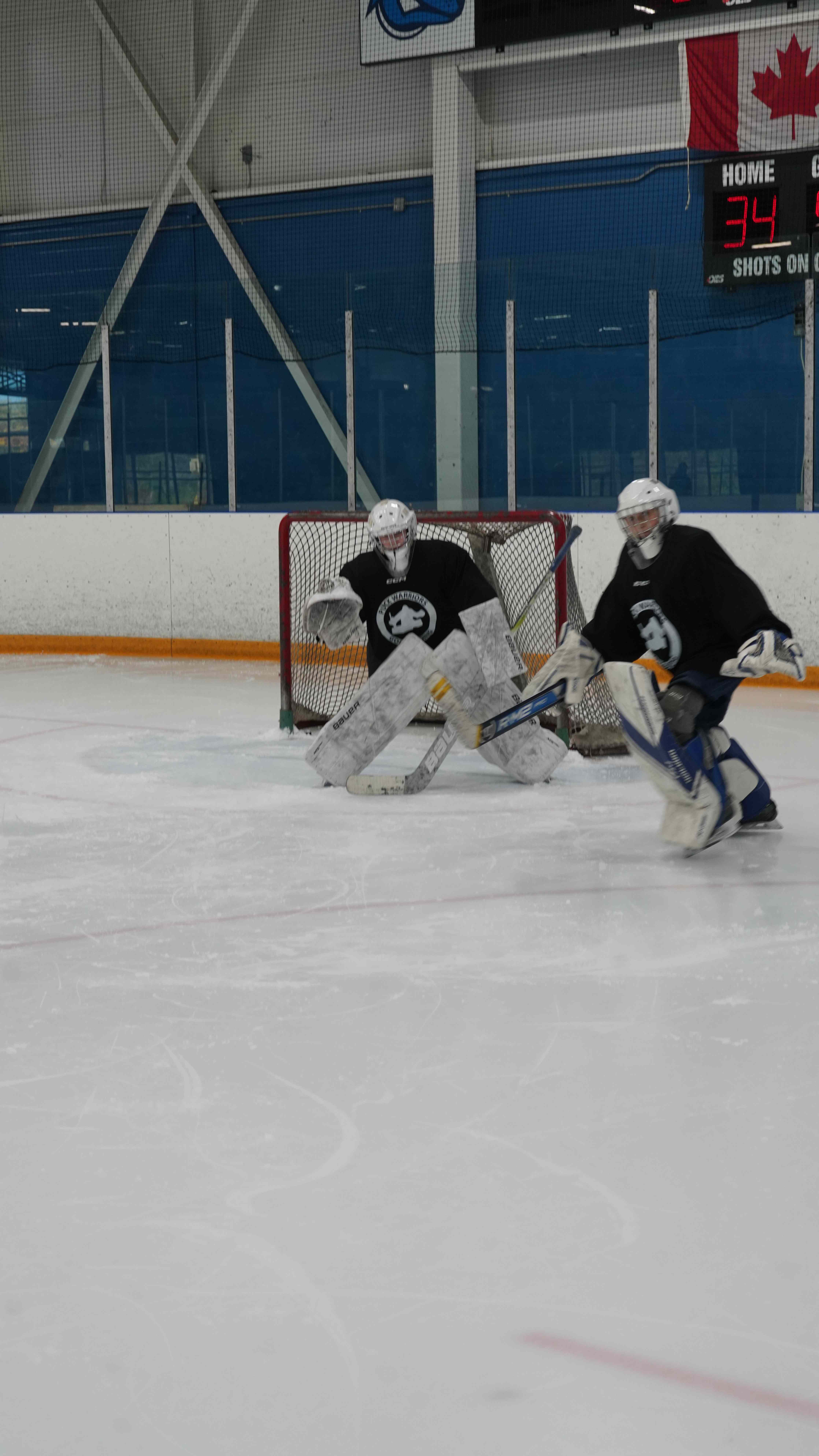 Two goalies working through a movement drill together on the ice