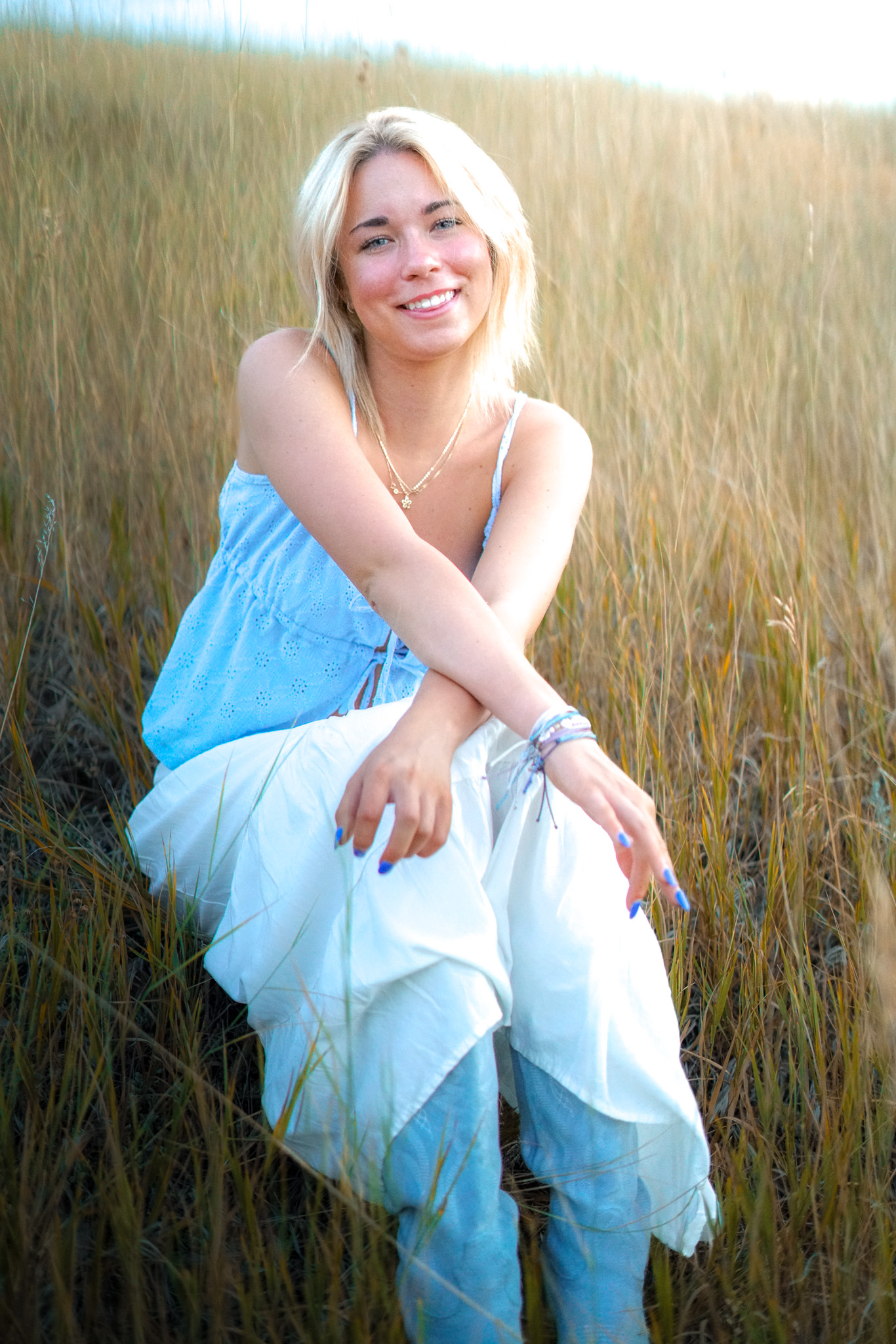 Senior portrait - blonde woman in blue top sitting in golden field