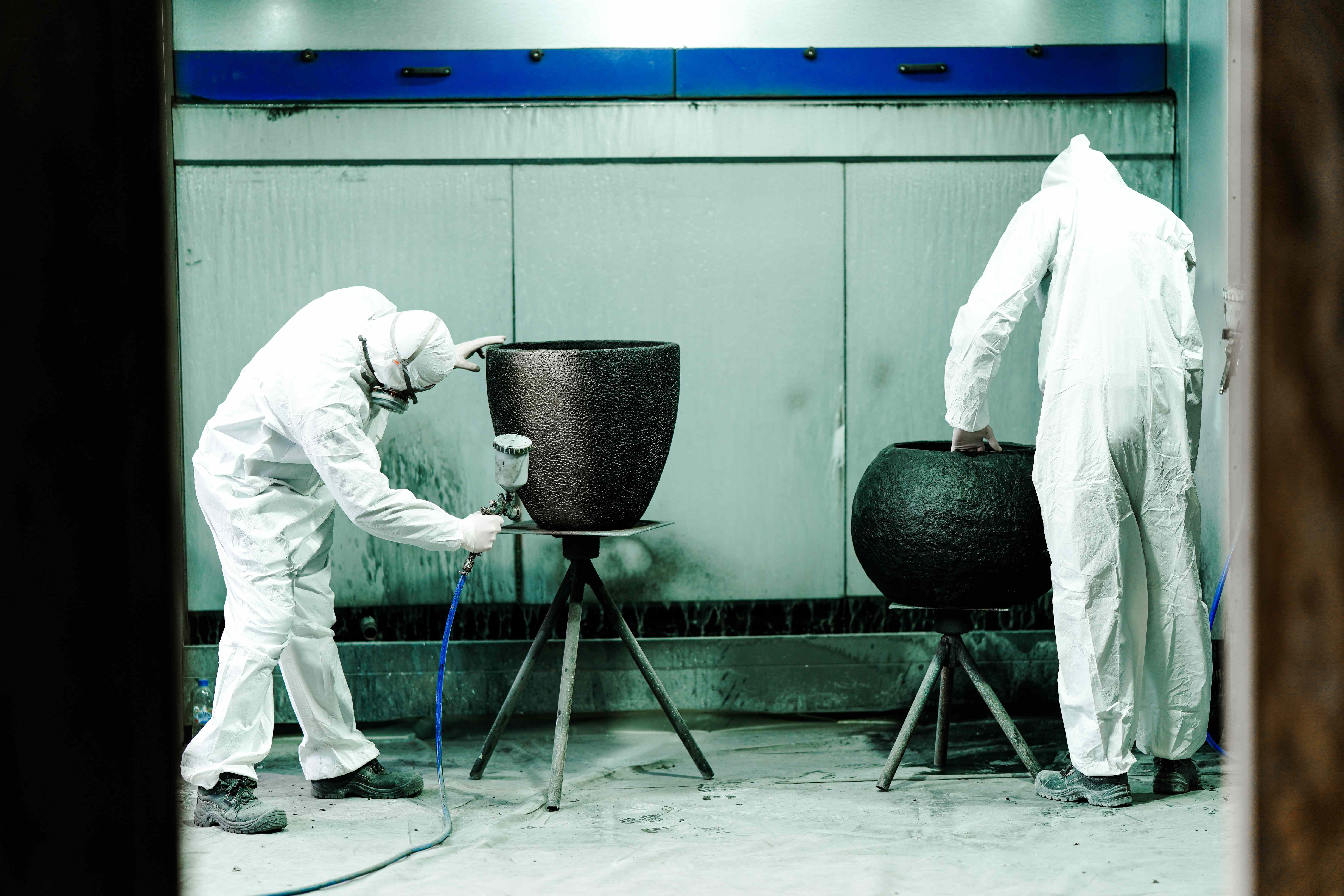 Due operai verniciano a spruzzo grandi fioriere nere in cabina