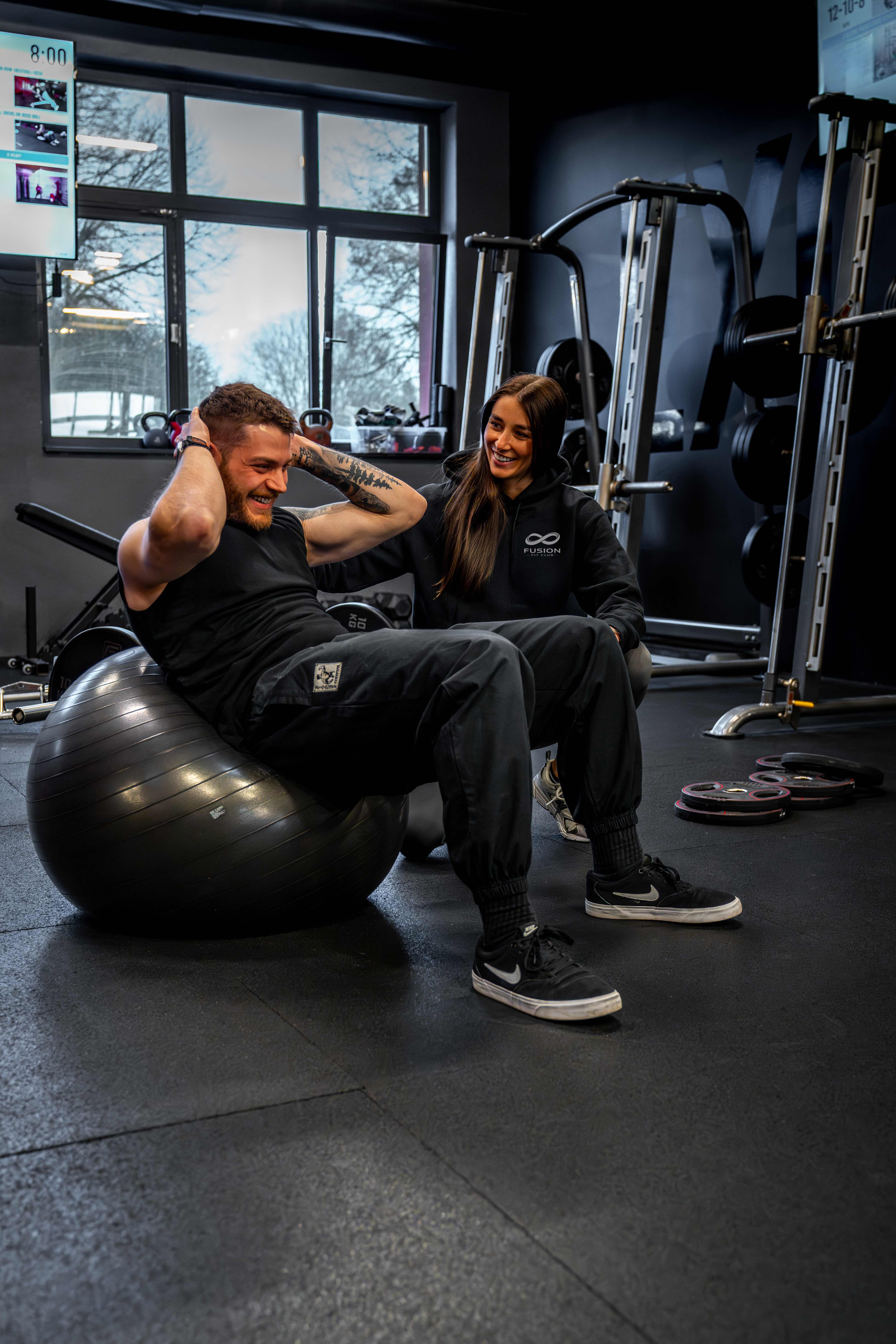 Coach begleitet einen Trainierenden persönlich bei einer Core-Übung auf dem Gymnastikball