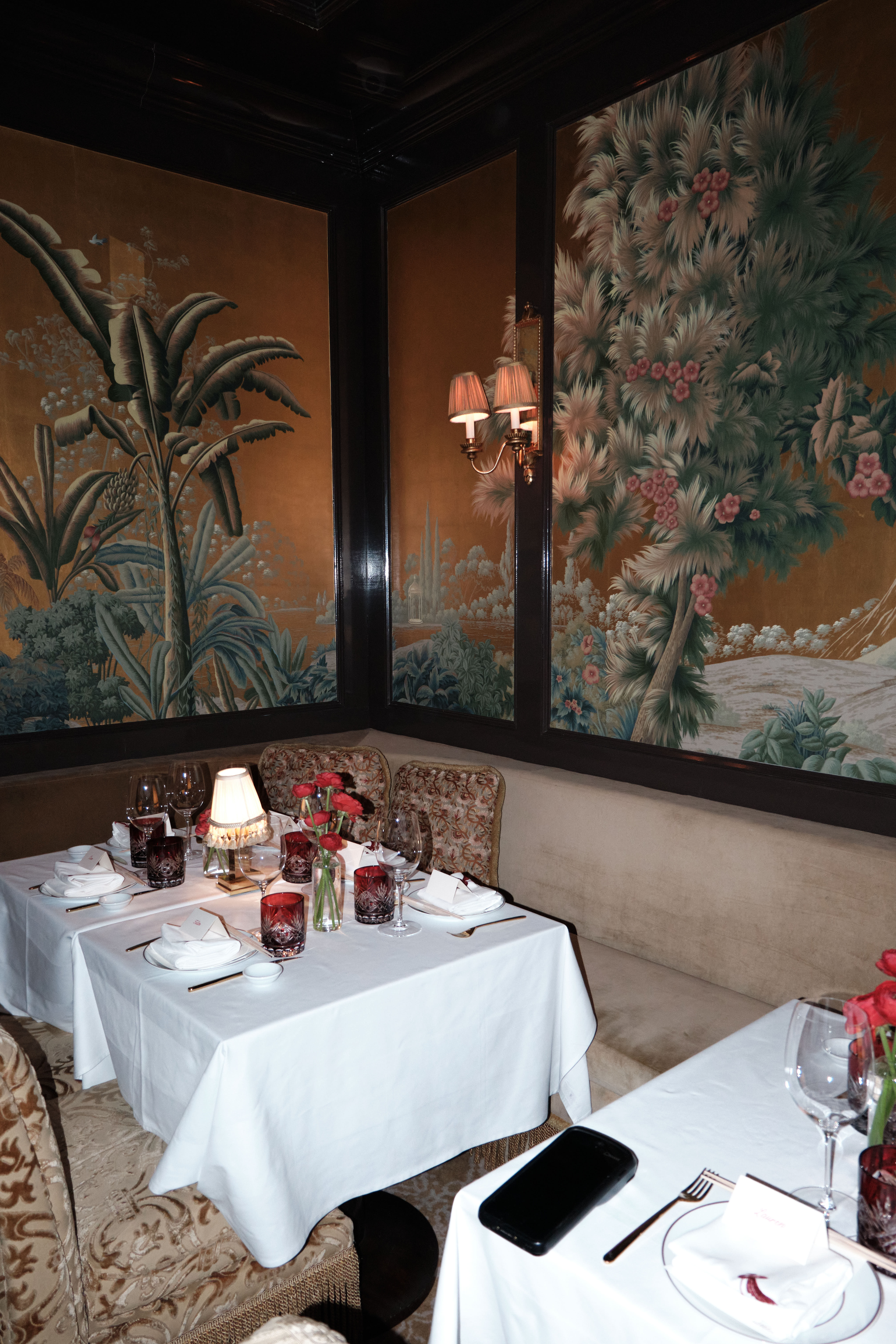 Elegant restaurant corner with chinoiserie tropical murals, white tables, and red crystal glassware