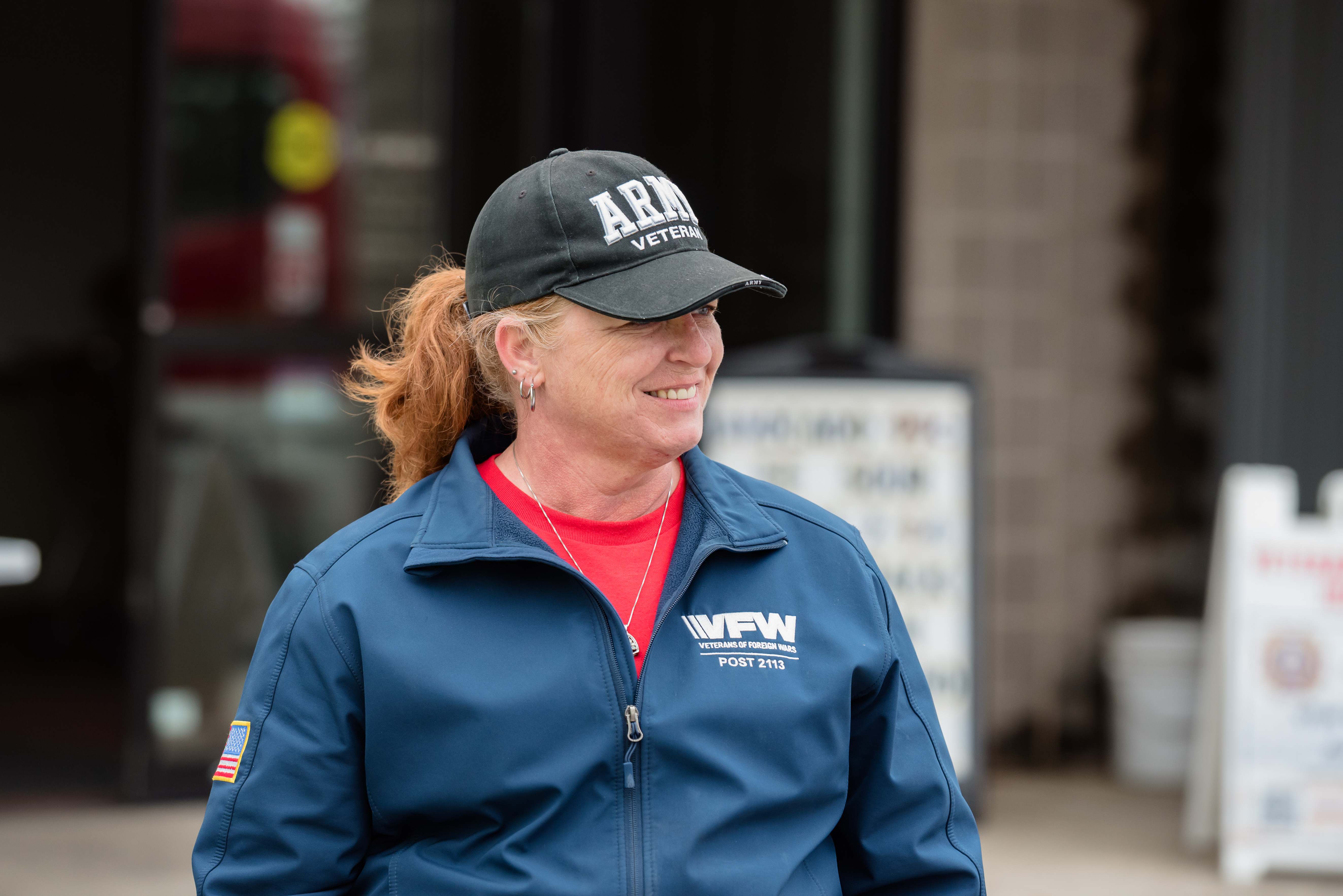 Female Army veteran smiling in VFW Post 2113 jacket with American flag patch