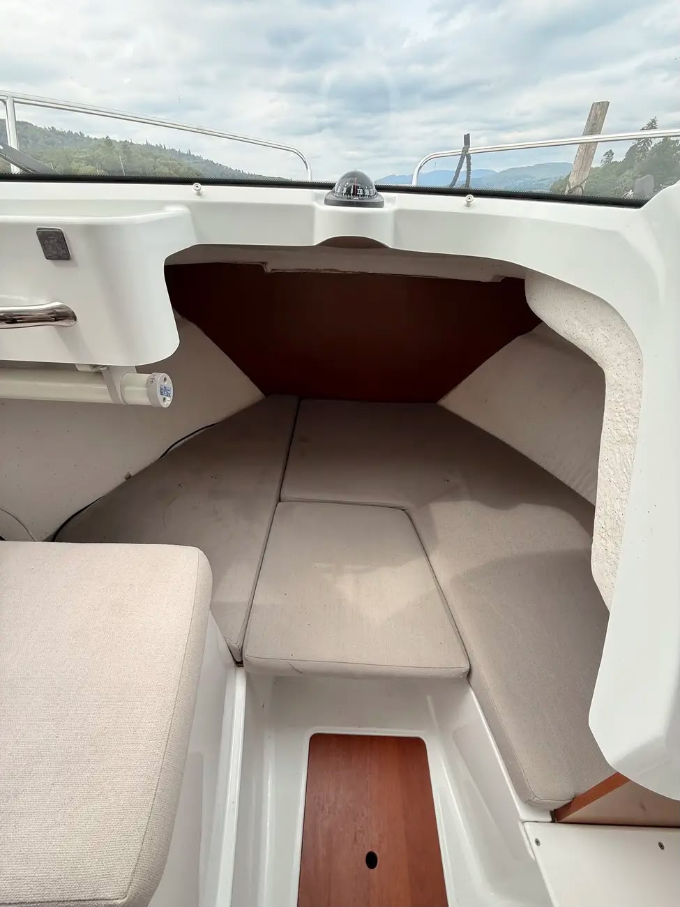 The forward berth with beige cushions and a mounted compass