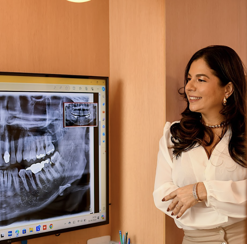 Dra. Thaís Halla Nery ao lado de monitor com radiografia panorâmica
