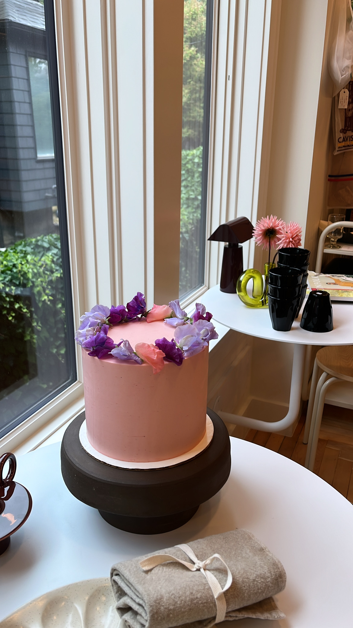 Pink cake with purple and pink sweet pea flowers on black ceramic stand