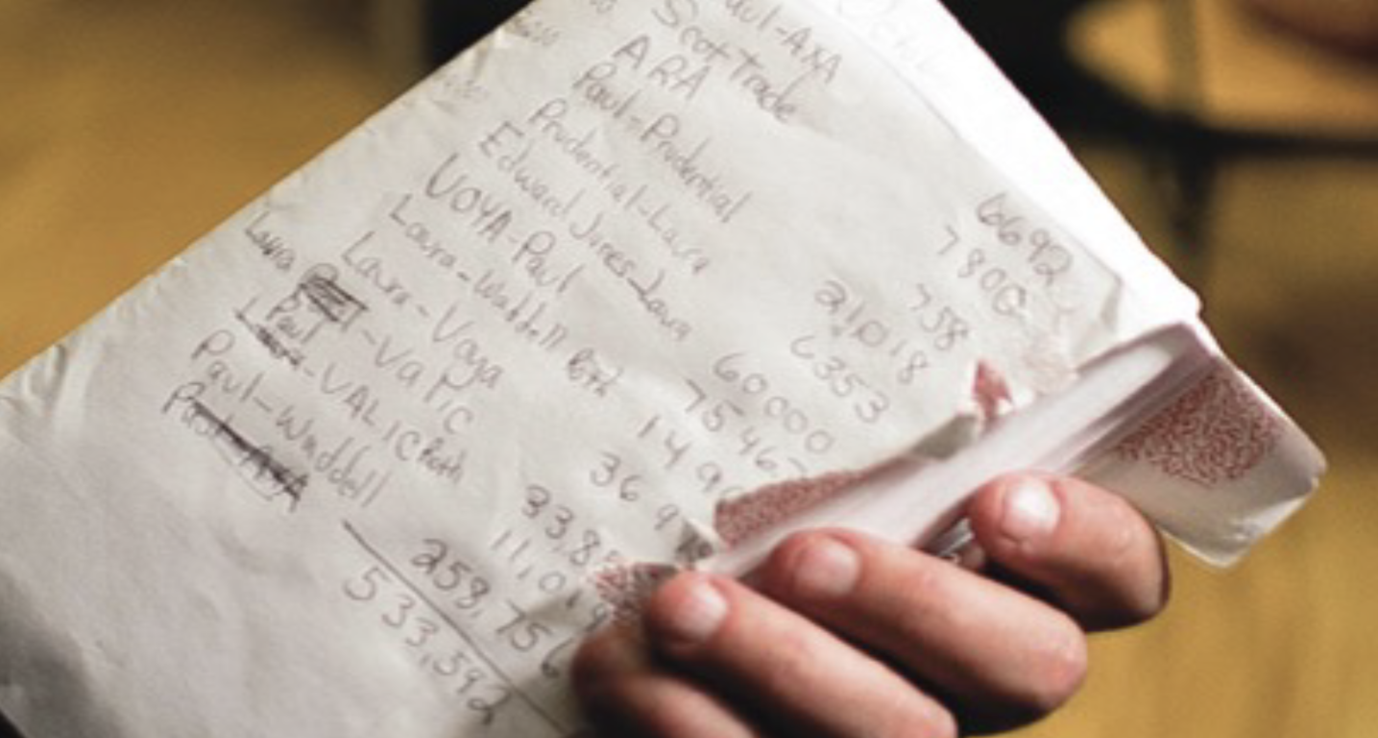 A close-up photo of a hand holding a worn, torn envelope covered in handwritten account names and balances — a list of eleven retirement accounts scattered across brokerages.