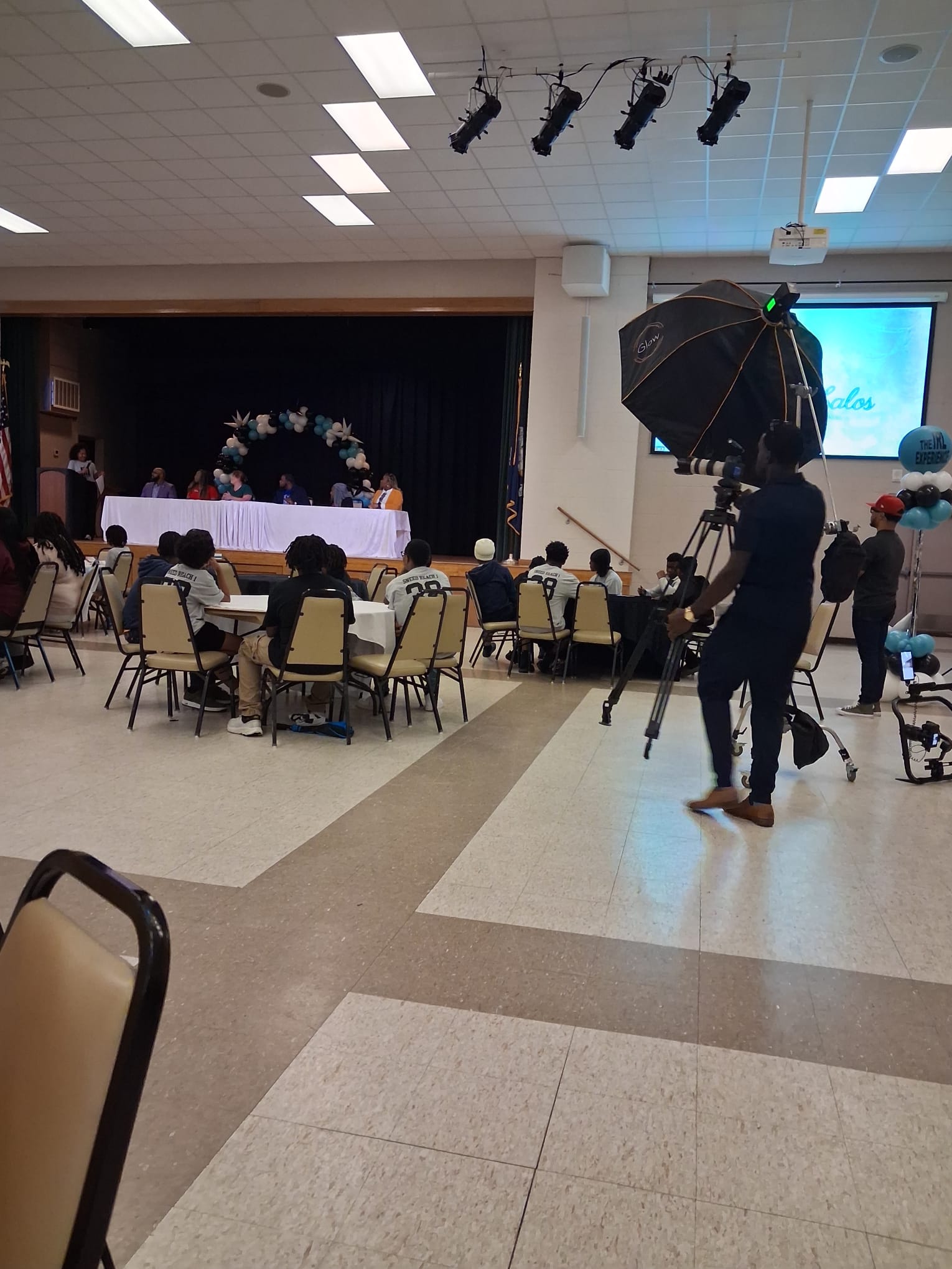 Panel discussion on stage with youth seated at tables during the event