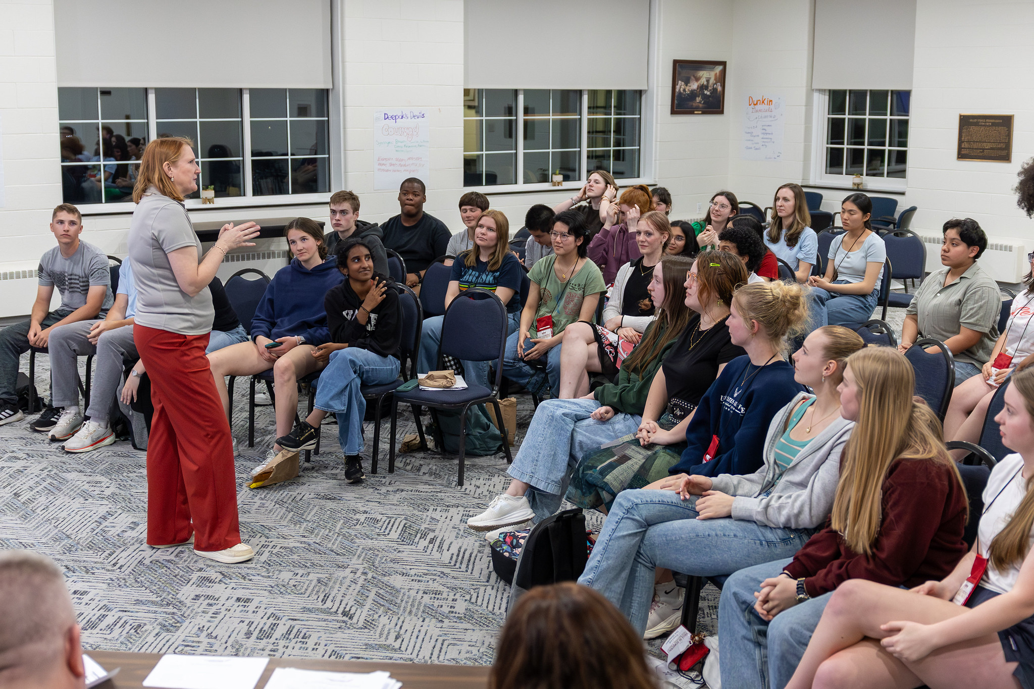 A presenter speaking to a large group of high school students seated in a community room during an educational outreach session
