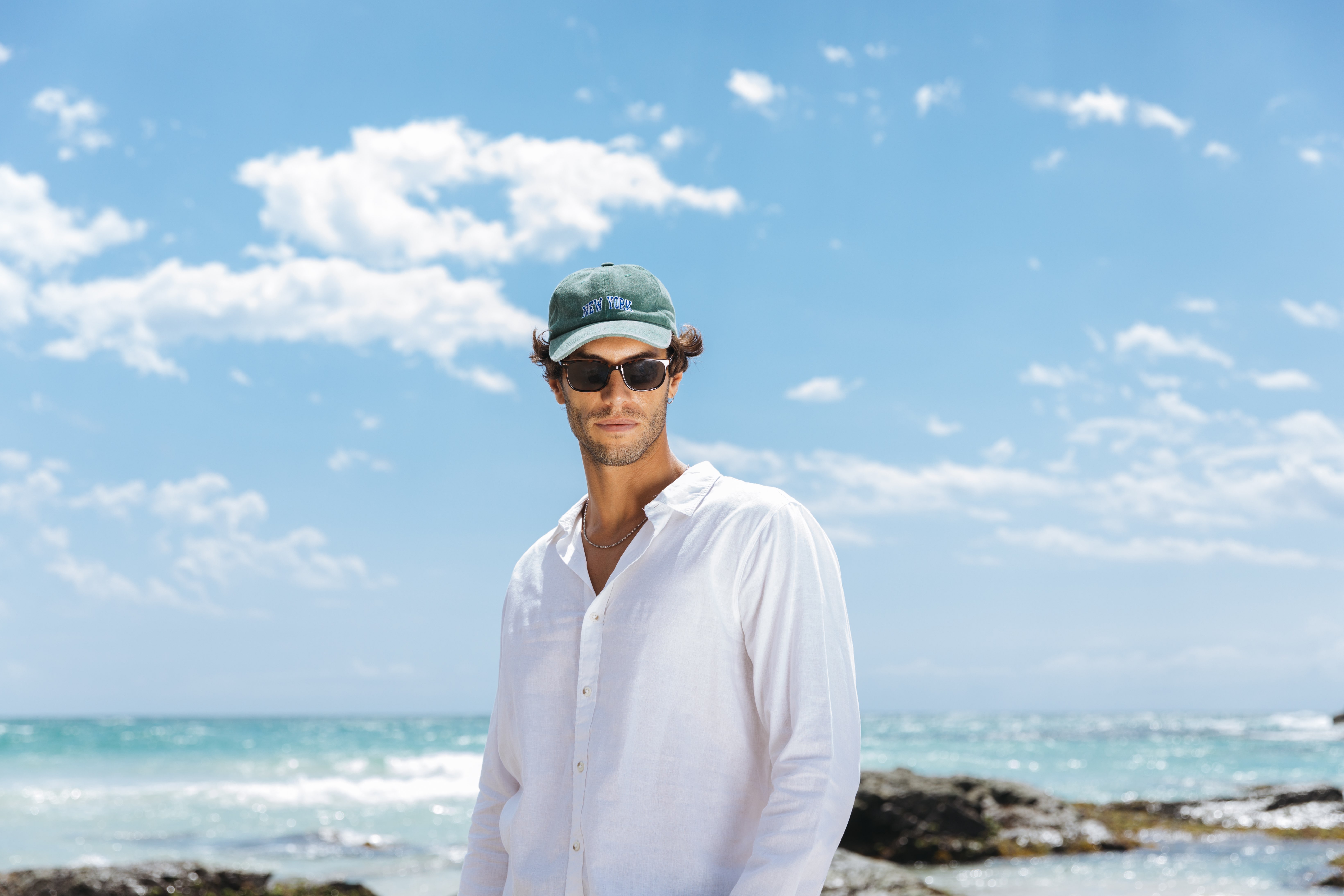 Elias in white linen shirt green cap coastal beach