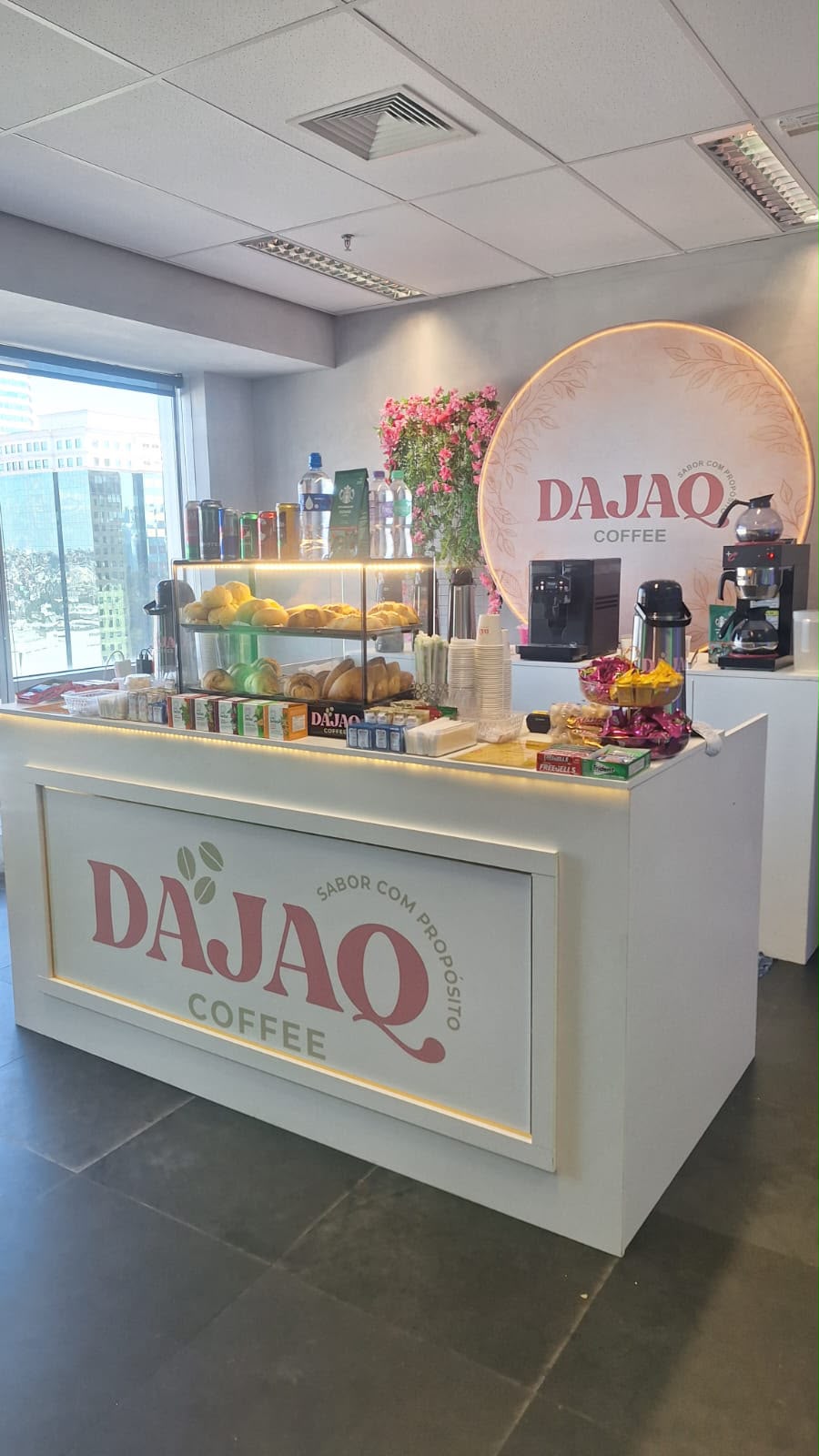 Estação de café DAJAQ com balcão branco, flores e máquinas de café em espaço de evento