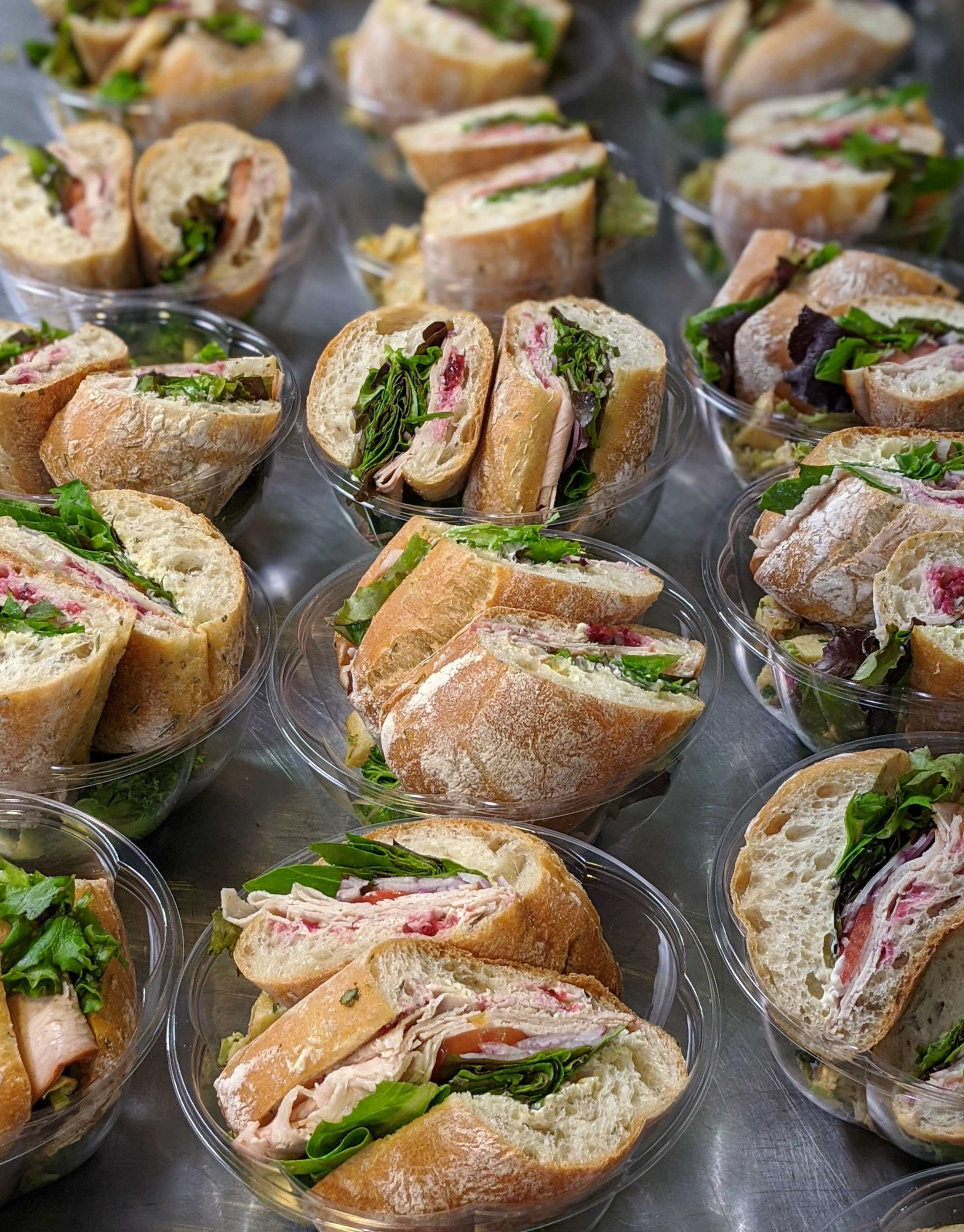 Rows of freshly prepared turkey and cranberry baguette sandwiches packaged in clear containers