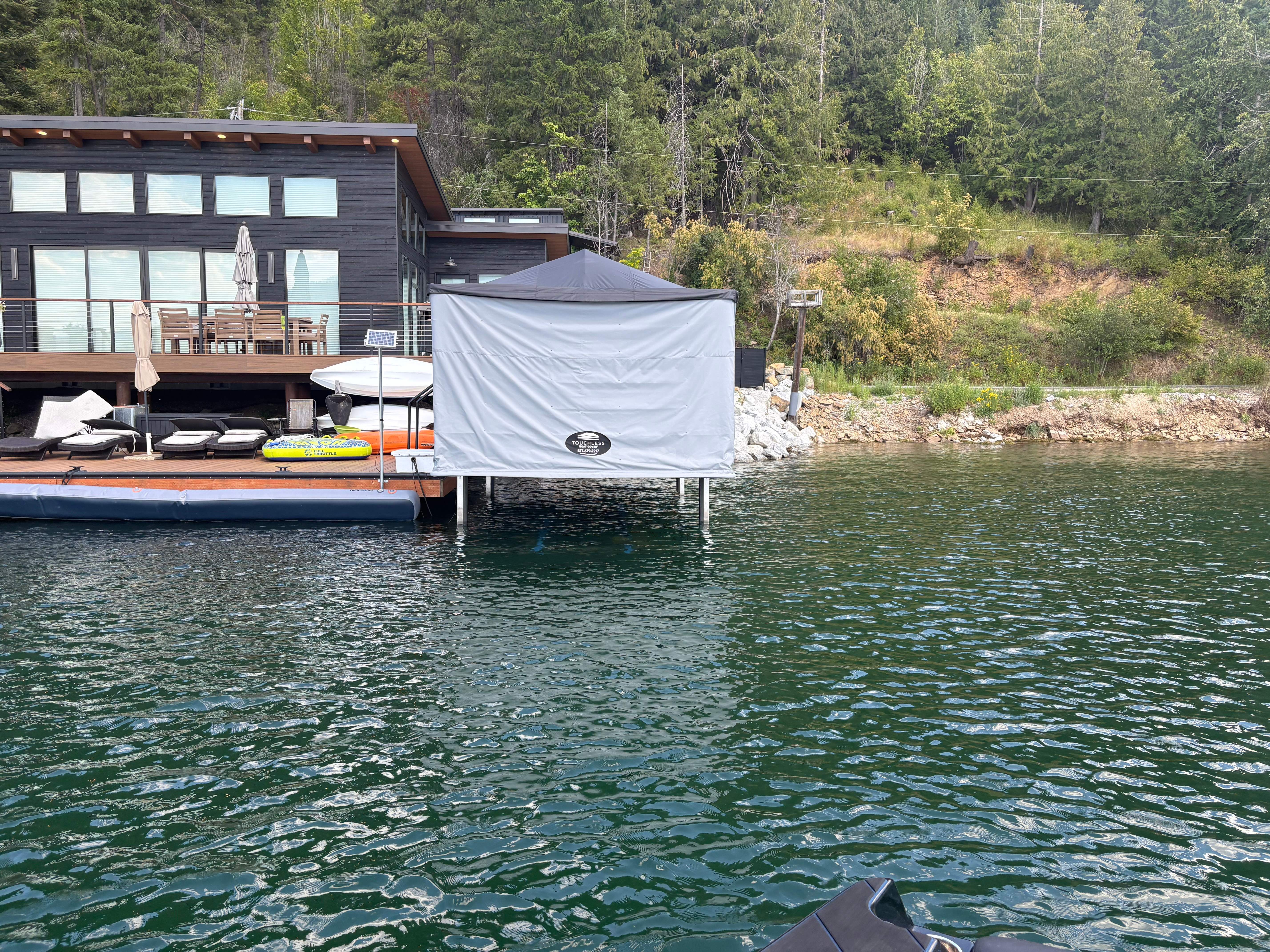 Touchless Cover boathouse enclosure installed on a lake dock with a luxury waterfront home in the background