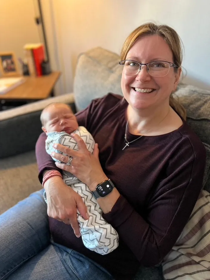 Pynne Floresca, RN, BSN, IBCLC, smiling while cradling a sleeping newborn