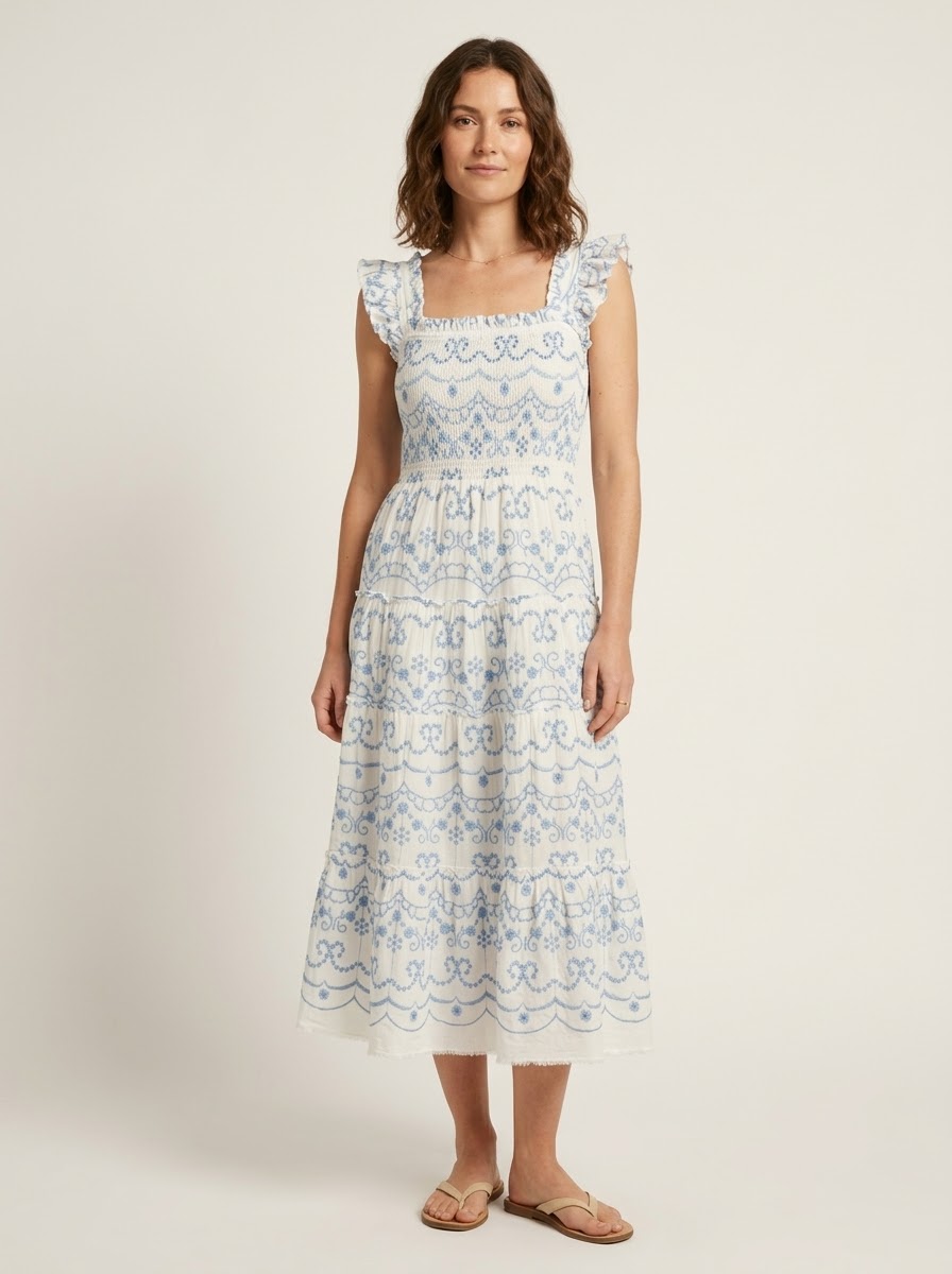 Model wearing an ivory tiered midi dress with powder-blue embroidery and ruffled straps.