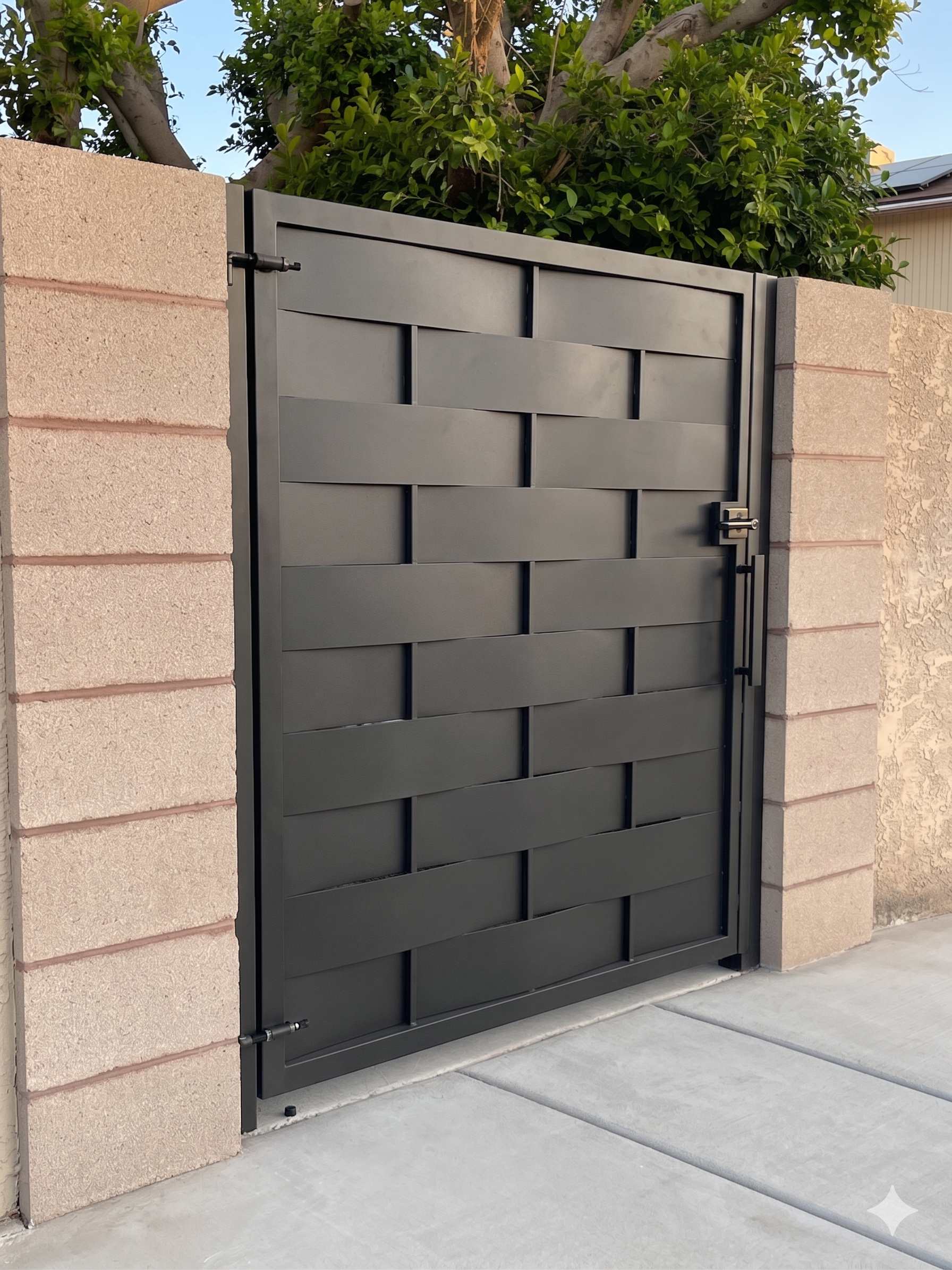 Woven basket pattern side gate in matte black between cinder block walls