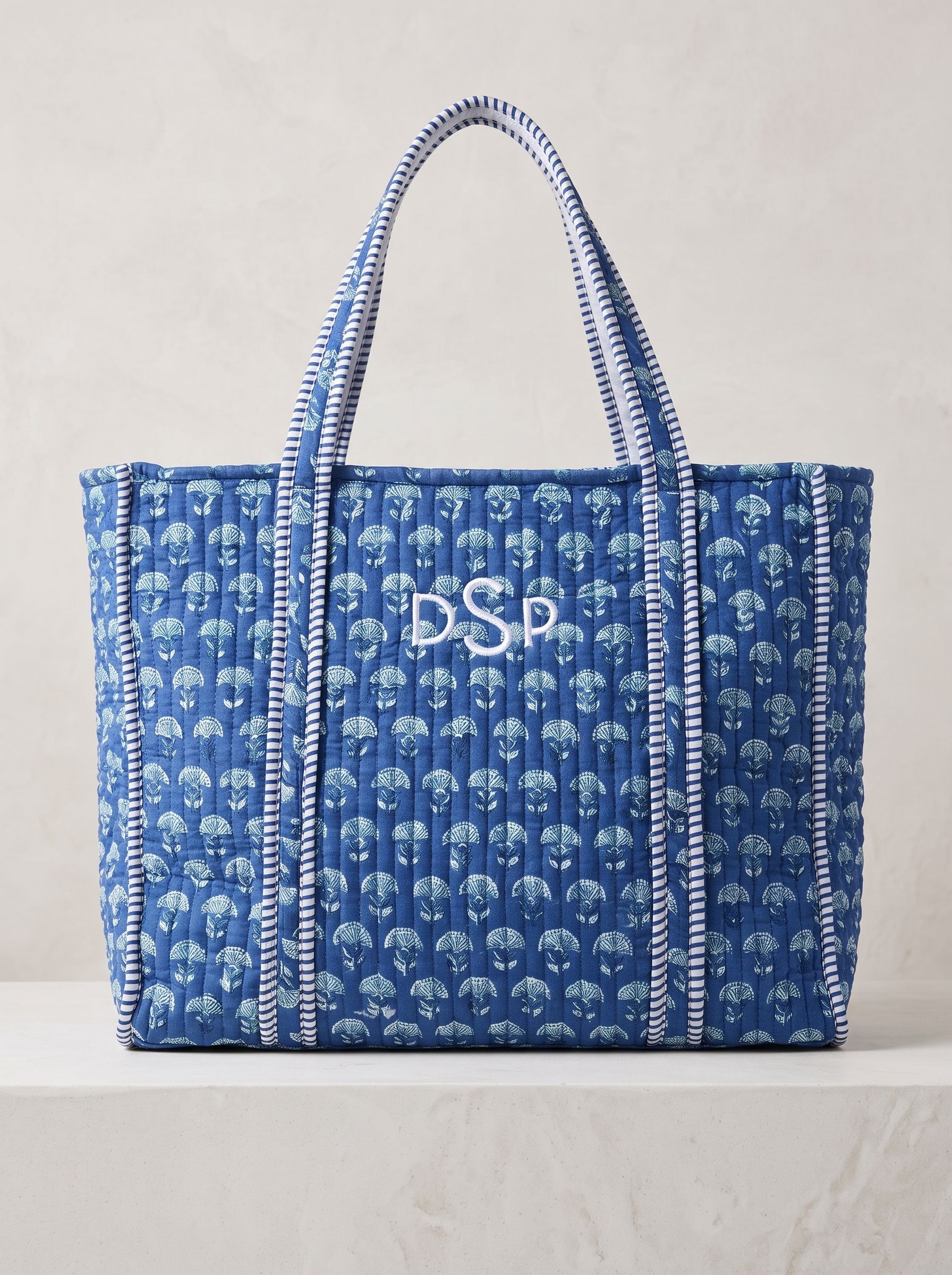 Made from cotton with a deep blue floral print, contrast handles, and quilted texture.