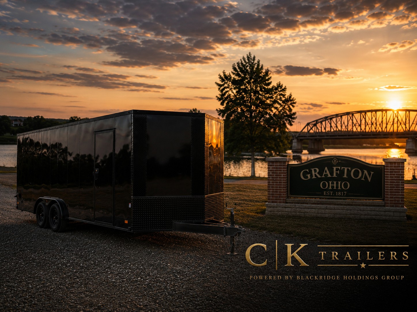 Black CK Trailers enclosed trailer parked near the Grafton Ohio Est. 1817 sign by the river bridge at golden hour