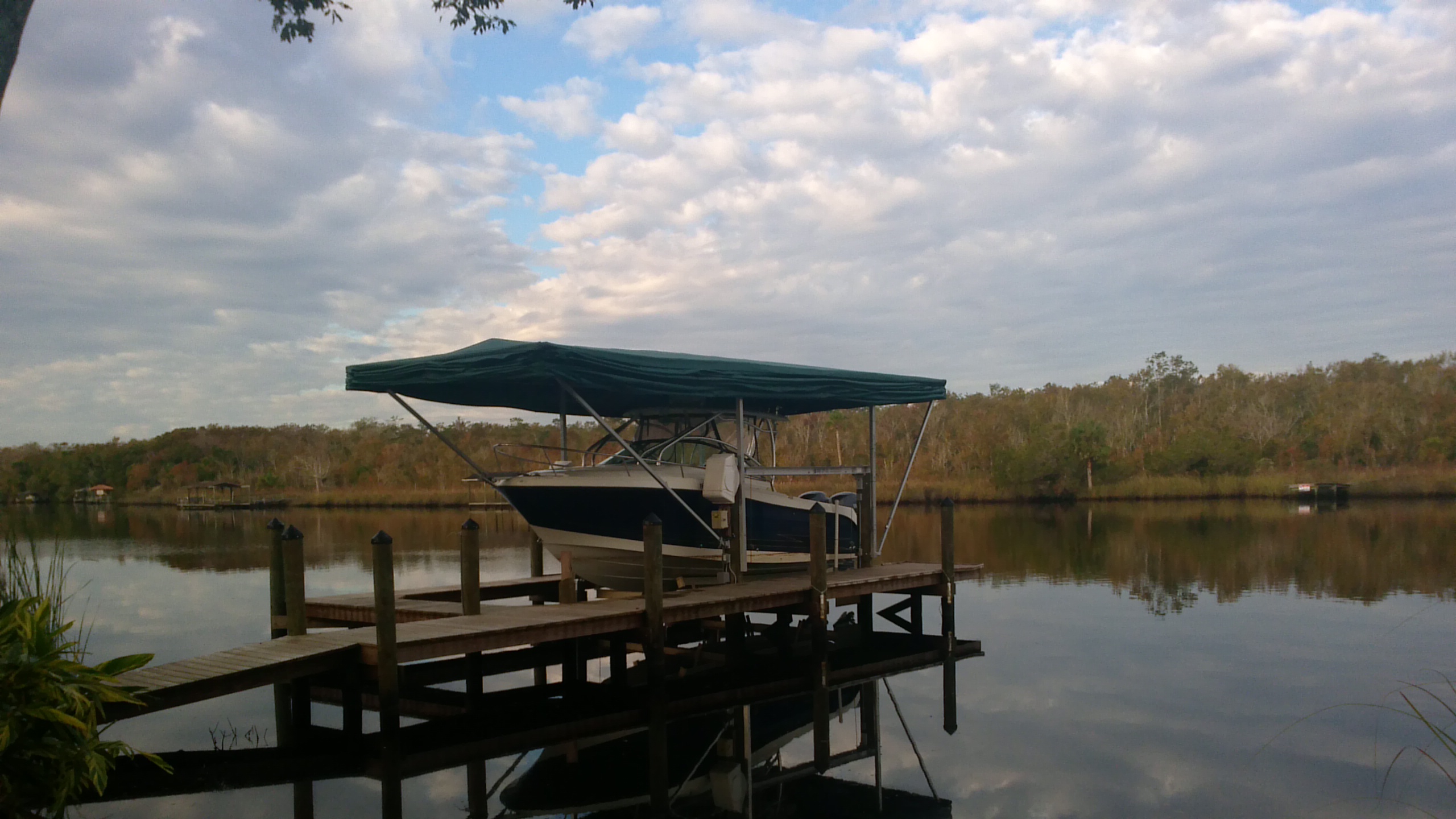 Green Touchless Cover open over a boat on a river dock surrounded by trees