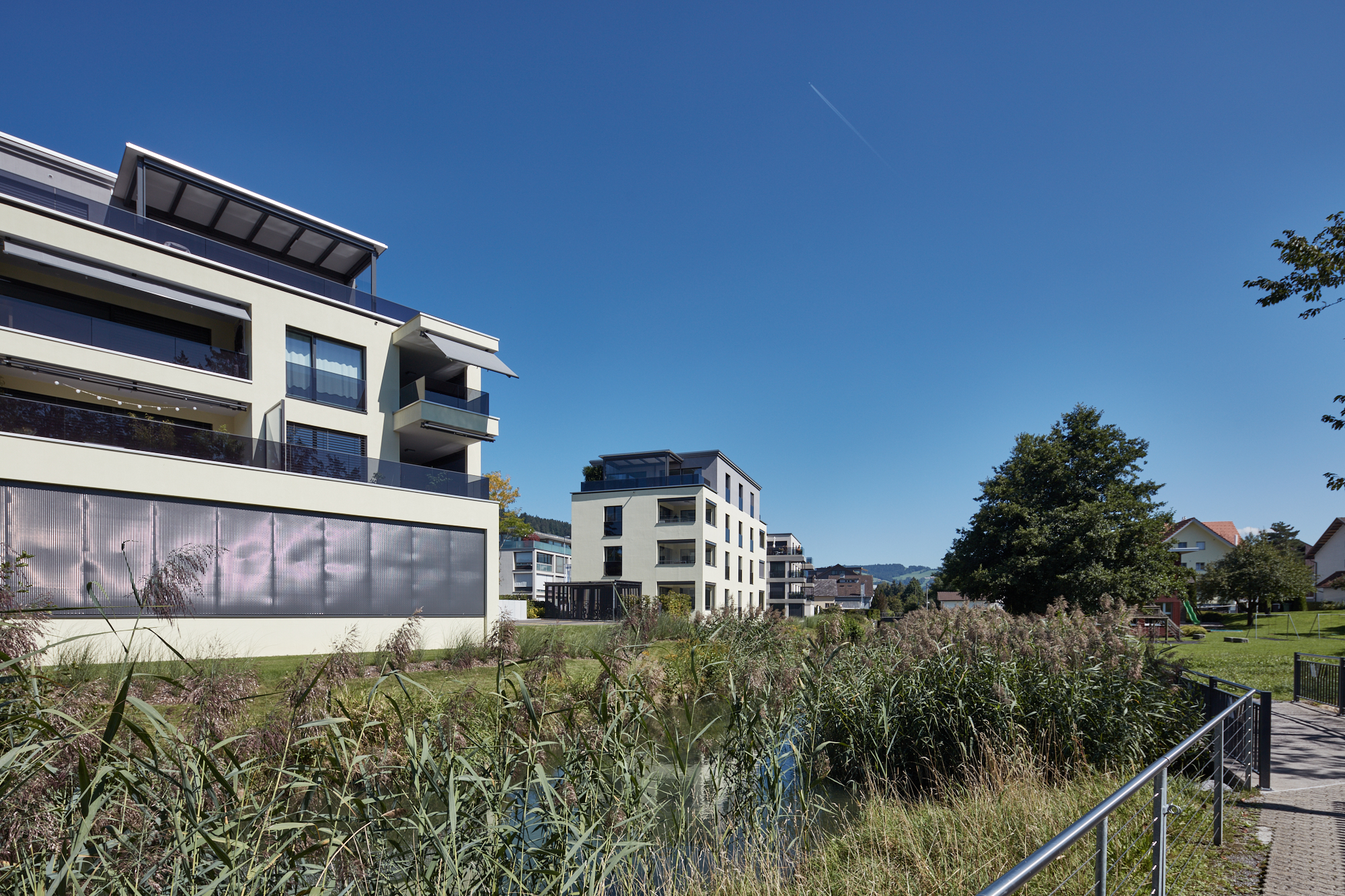 Moderne Wohnanlage am Wasser mit begrüntem Ufer und Spielplatz
