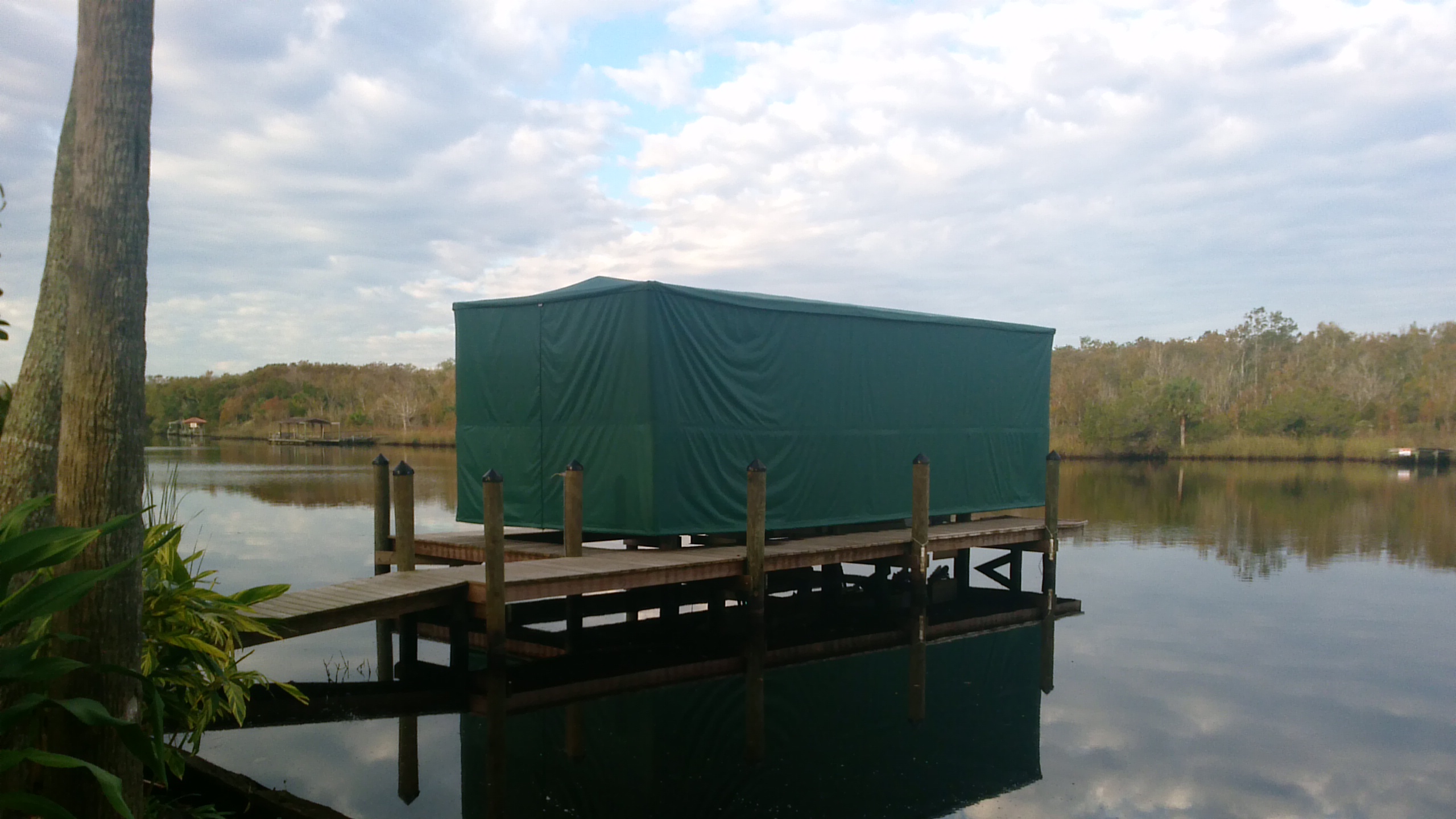 Green Touchless Cover fully closed over a boat lift on a wooded river dock