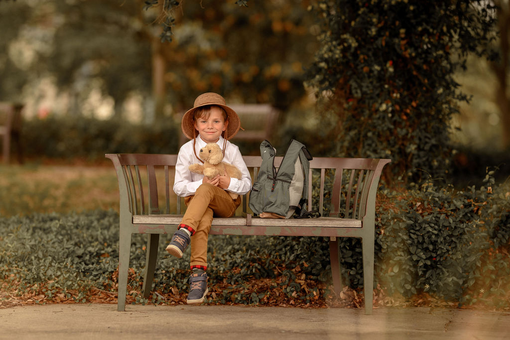 Young explorer Beckett sitting on a park bench with his teddy bear and backpack