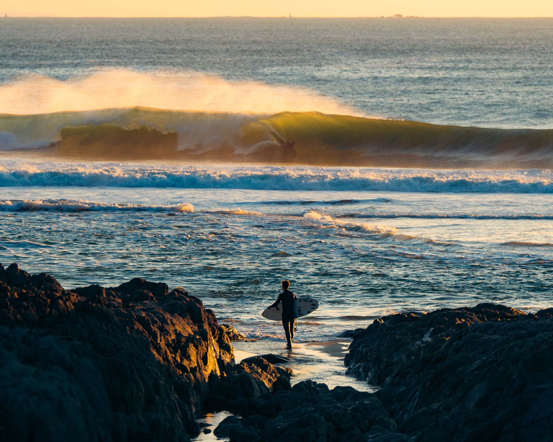 Surfer at sunset between rocks