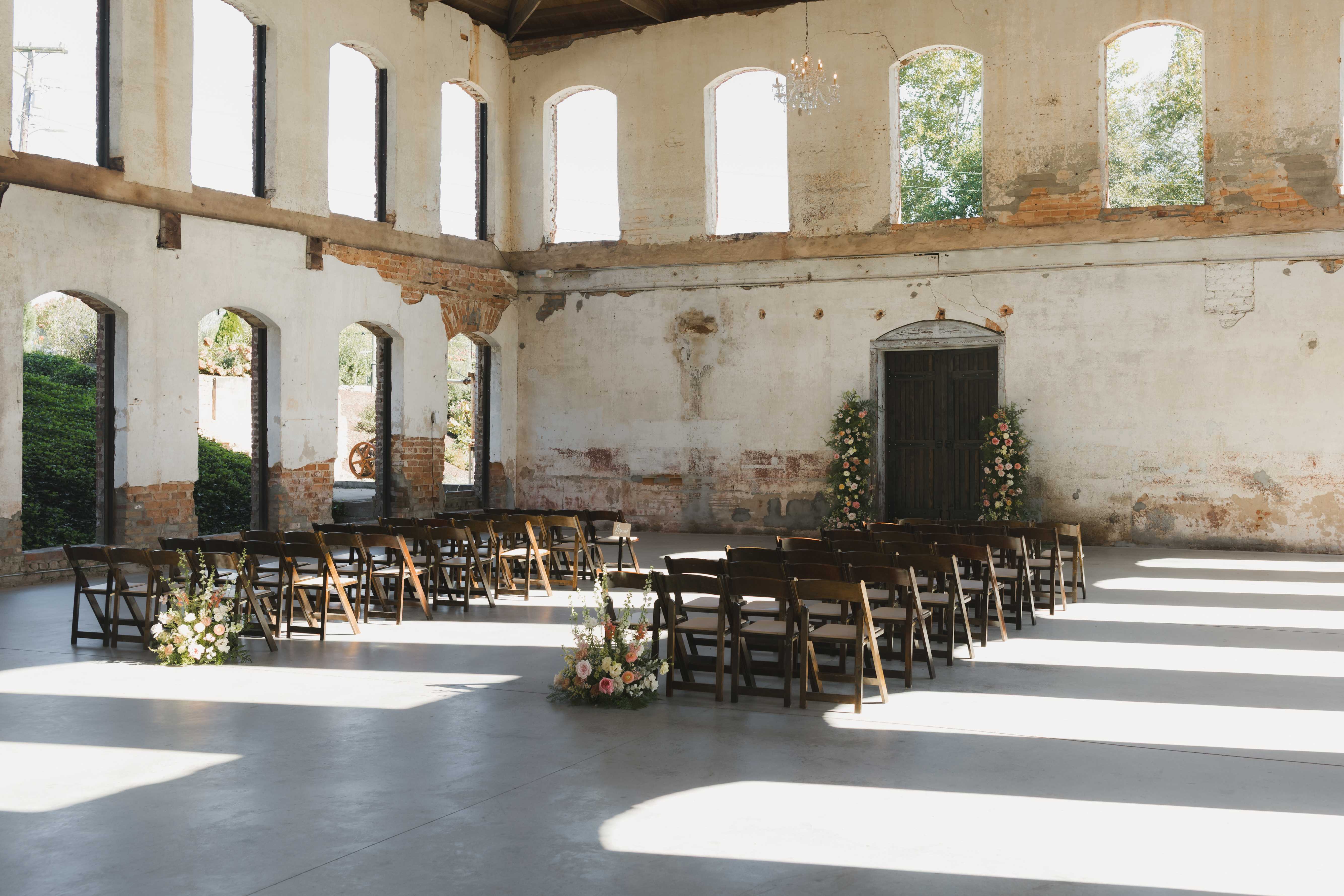 Restored industrial ruin wedding ceremony space with wooden chairs and florals