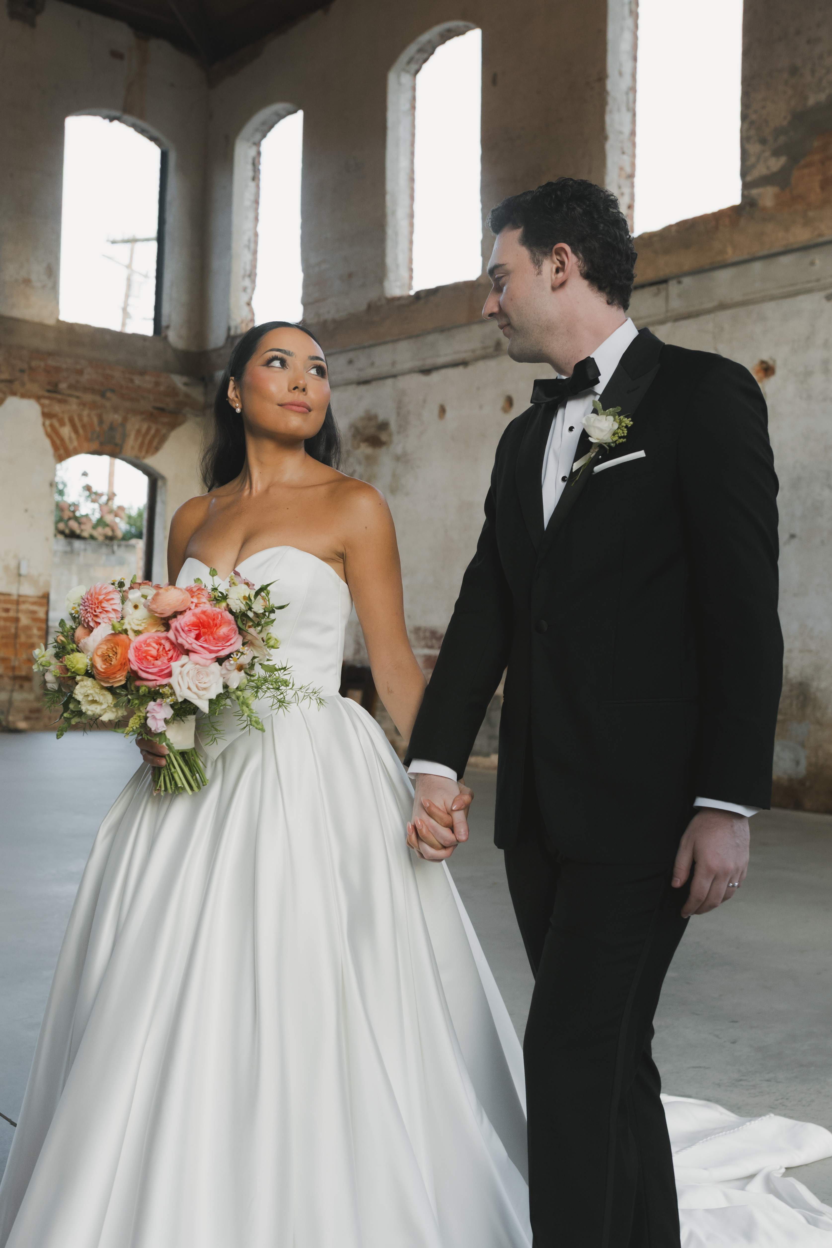 Bride and groom holding hands in a rustic brick venue with arched windows