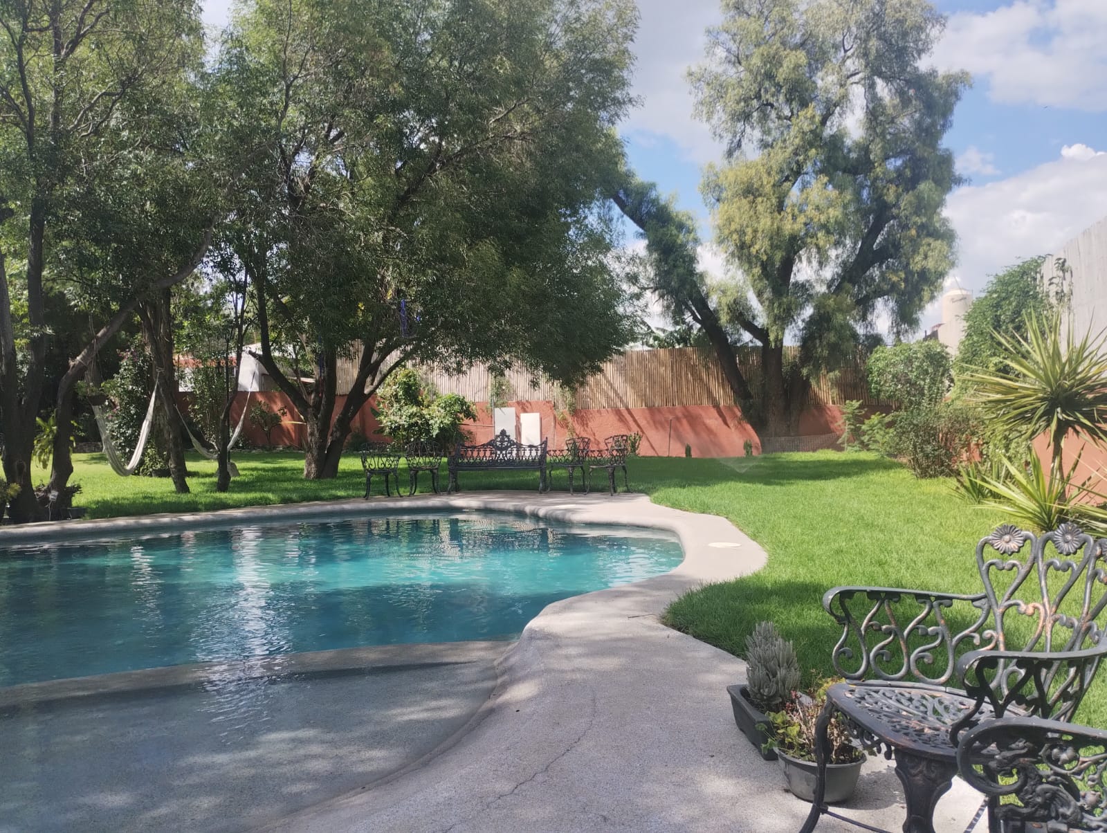 Alberca con bancas de hierro y jardin