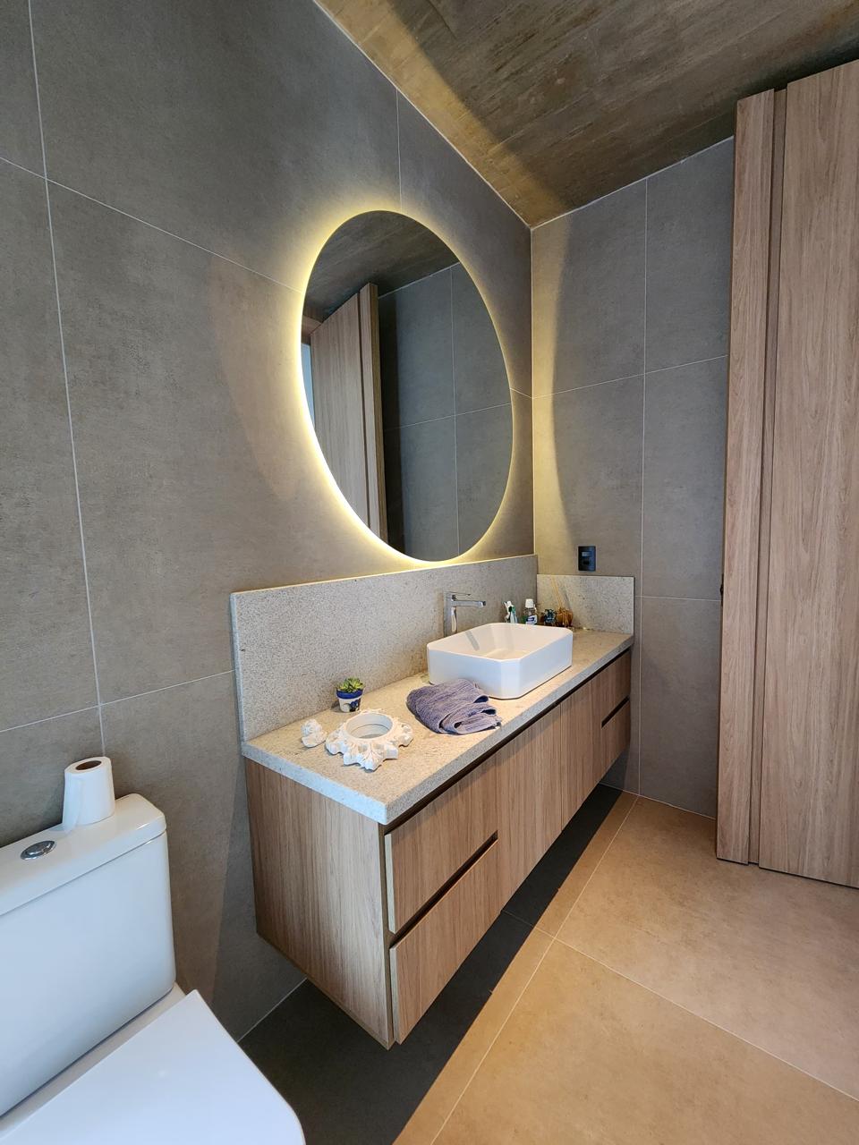 Banheiro sofisticado com espelho oval iluminado e revestimento em porcelanato