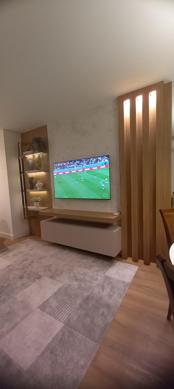 Sala de estar com painel de TV, ripas verticais iluminadas e prateleiras