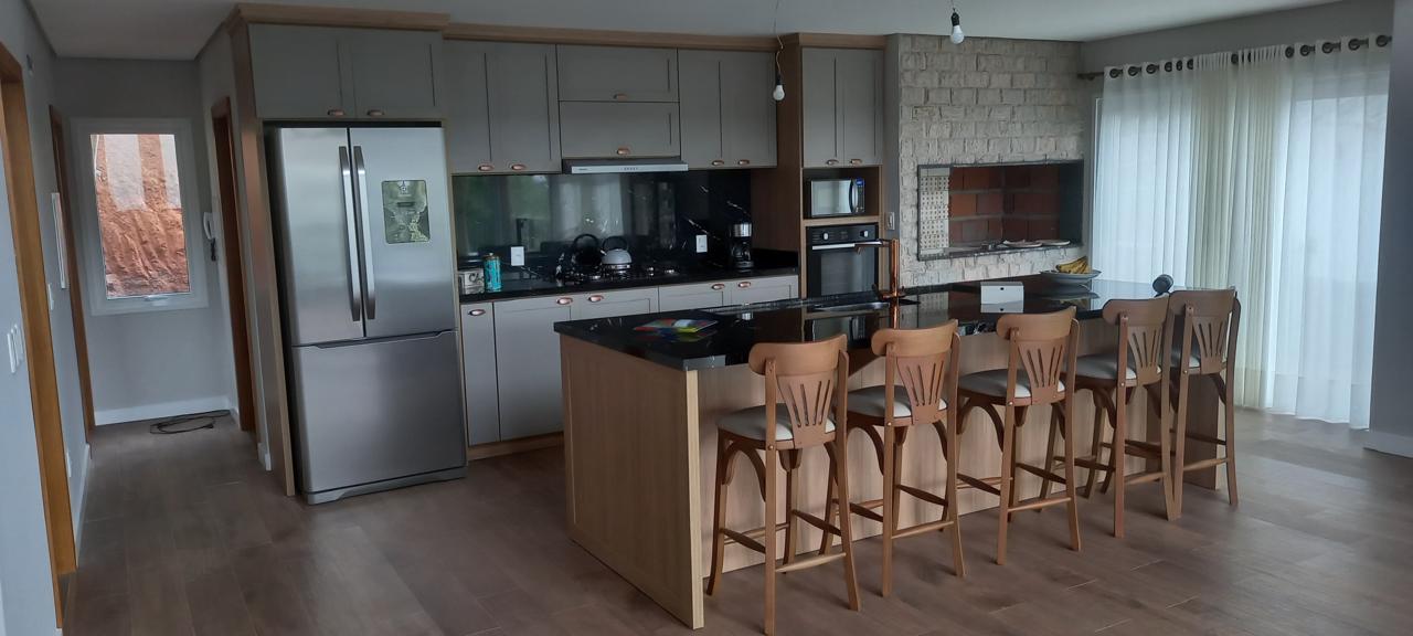 Cozinha moderna com ilha central, banquetas de madeira e parede de tijolos