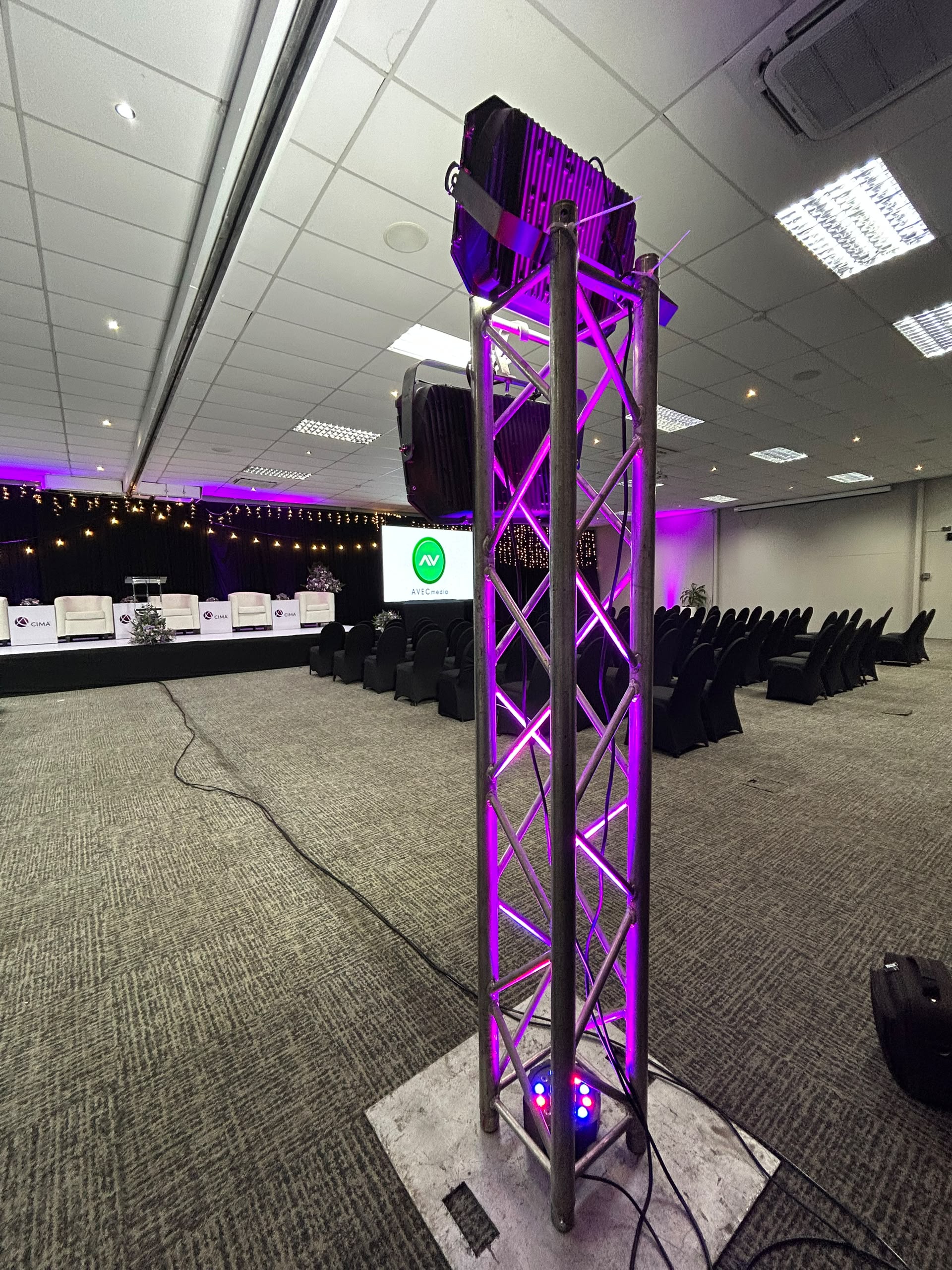 Large indoor event venue with purple LED-lit truss structure and professional staging
