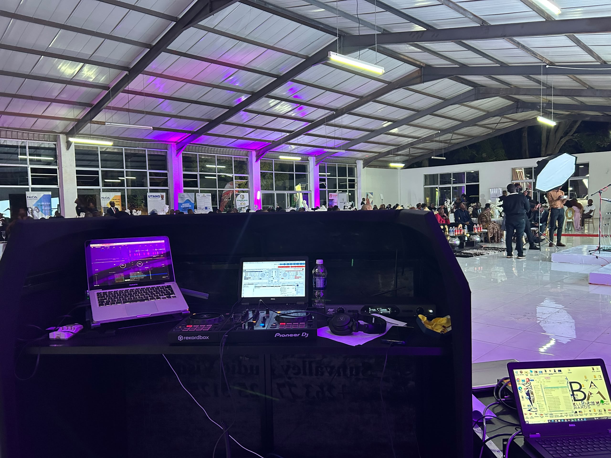 Professional DJ control booth with MacBook, Pioneer DJ equipment, and purple ambient lighting