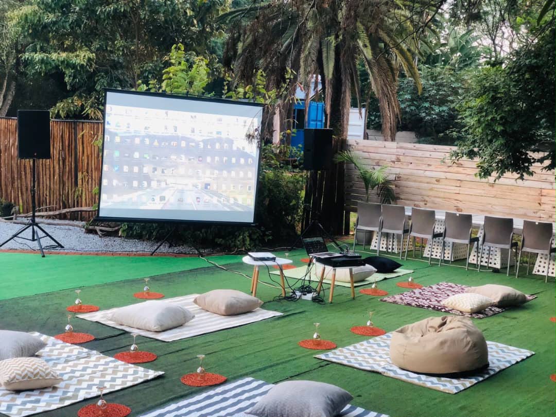 Outdoor garden event with projection screen, beige cushions on green carpet, intimate seating