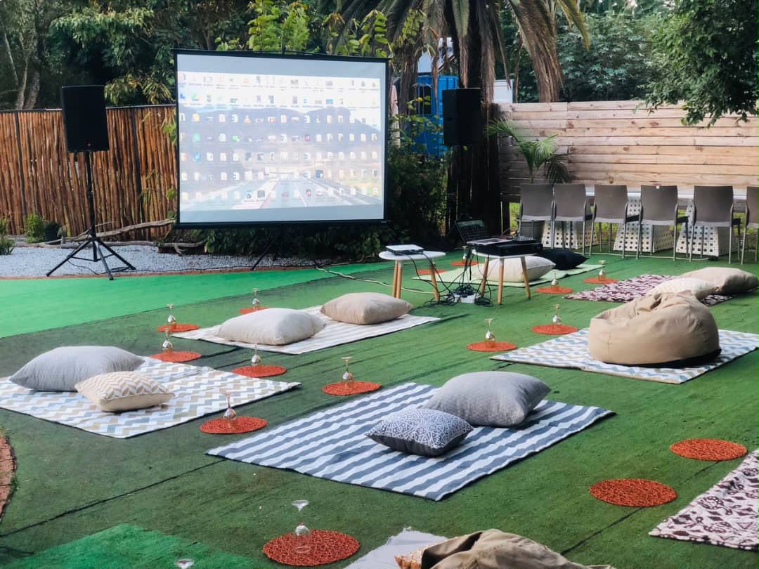 Outdoor garden event with projection screen, beige cushions on green surface, intimate venue setup