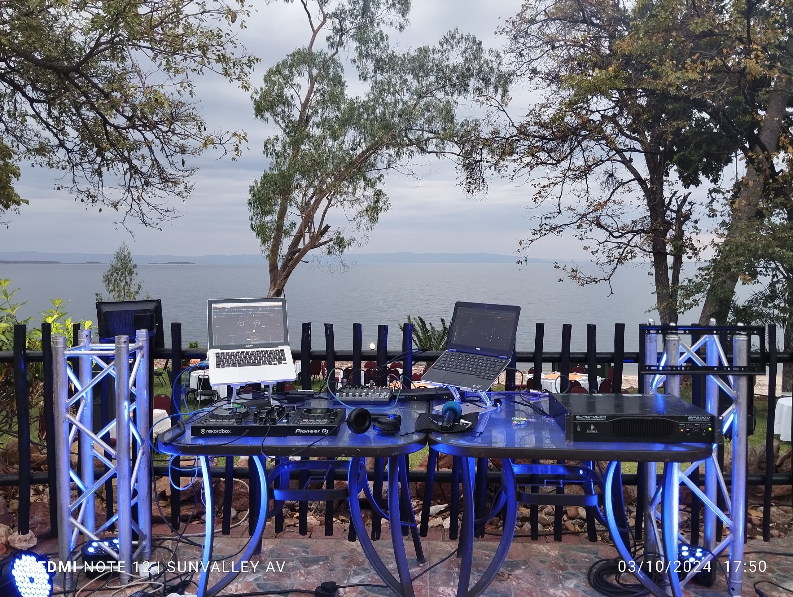 Outdoor DJ setup with blue truss lighting, Pioneer equipment, and lakeside backdrop
