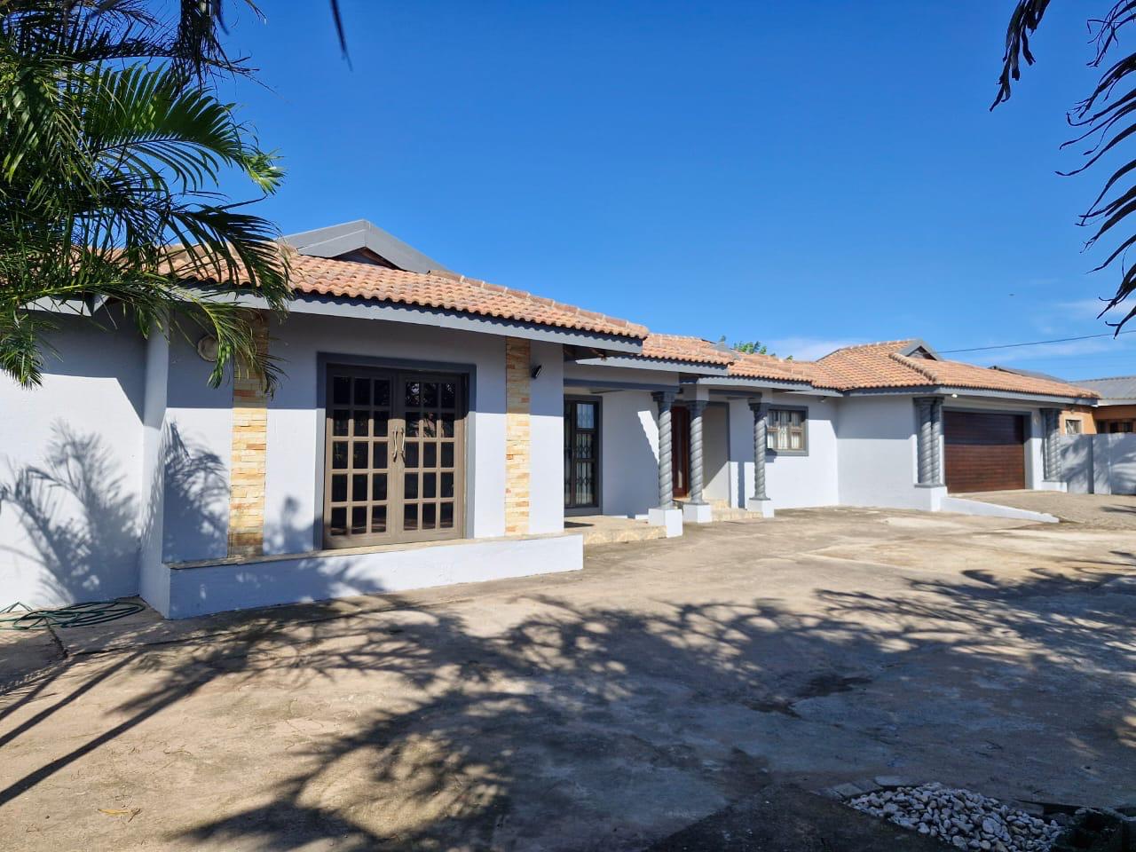 Front exterior of Ekwandeni Guest House with a tiled roof and palm trees