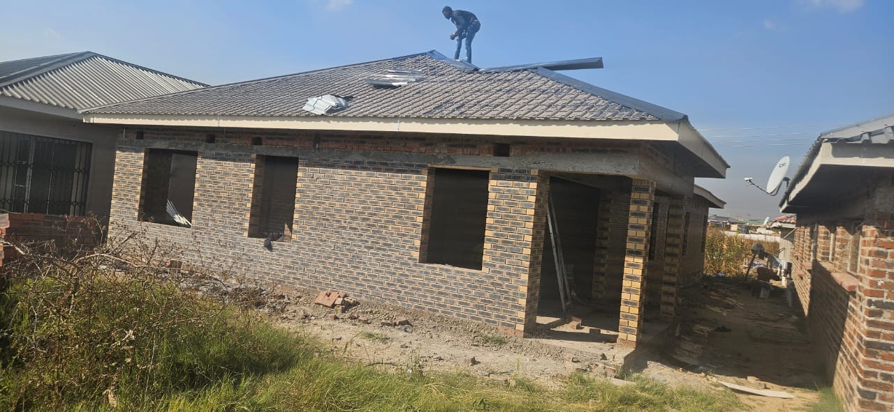 Roofing — worker finishing tiled roof on single-storey brick house
