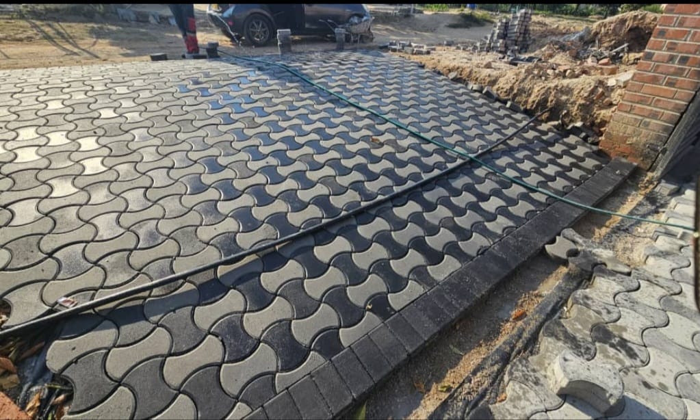 Paving — dark interlocking wave-pattern pavers being laid beside a brick wall