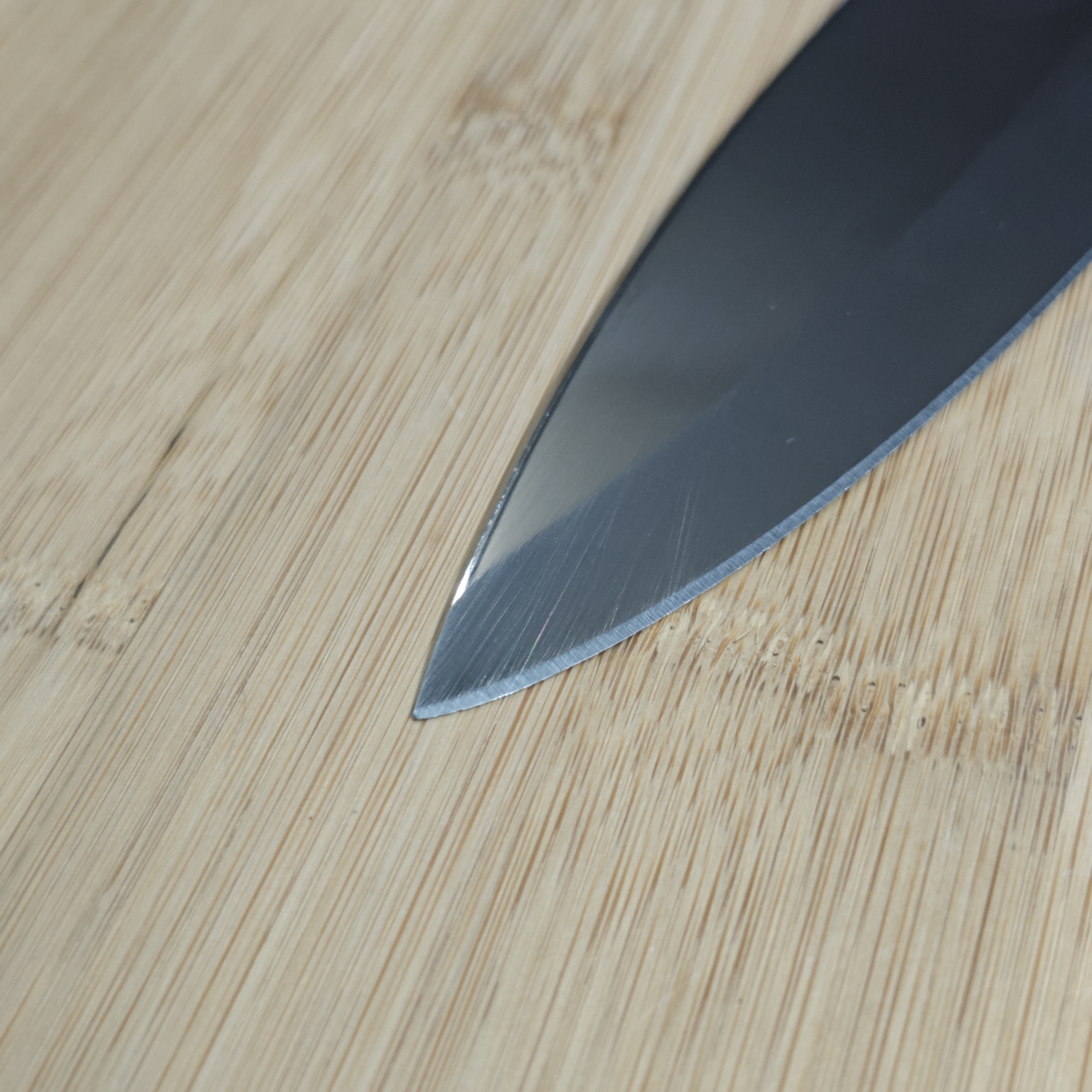 Knife tip on bamboo cutting board, visible edge wear and scratches before professional sharpening