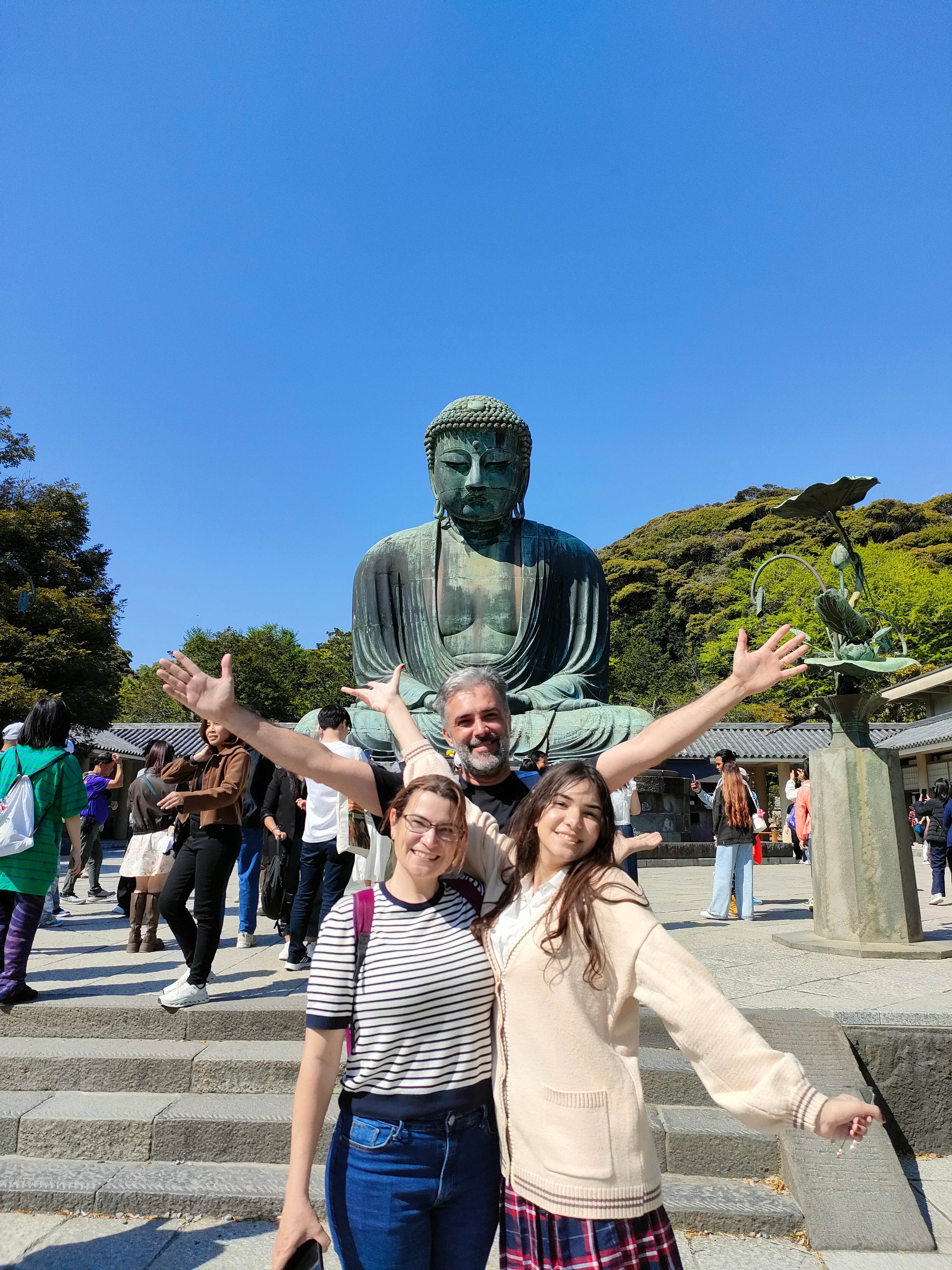 Happy family posing with arms raised in front of the Great Buddha (Daibutsu) in Kamakura