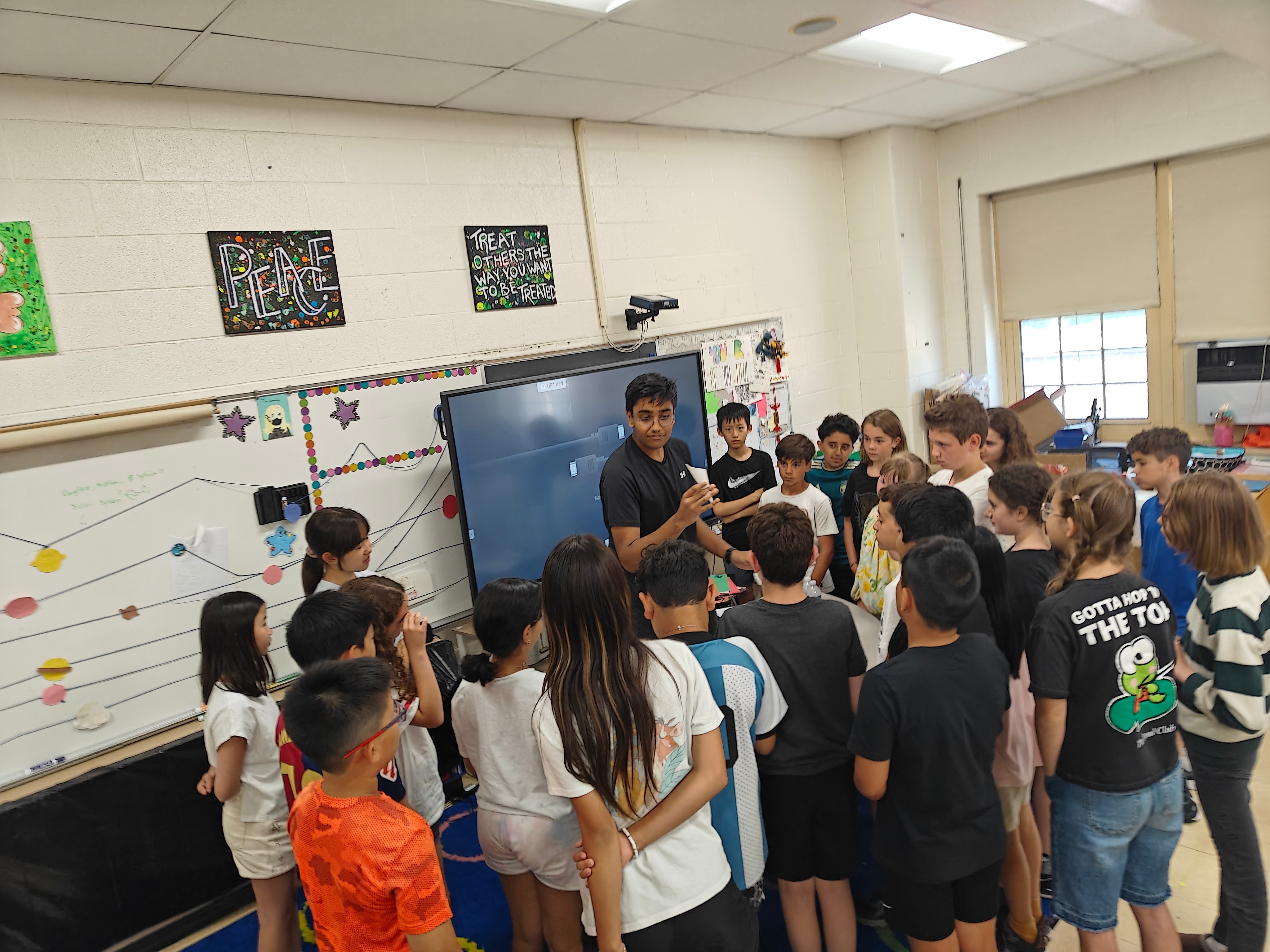 Student presenter leading a science demonstration in front of a smartboard for a group of elementary school students