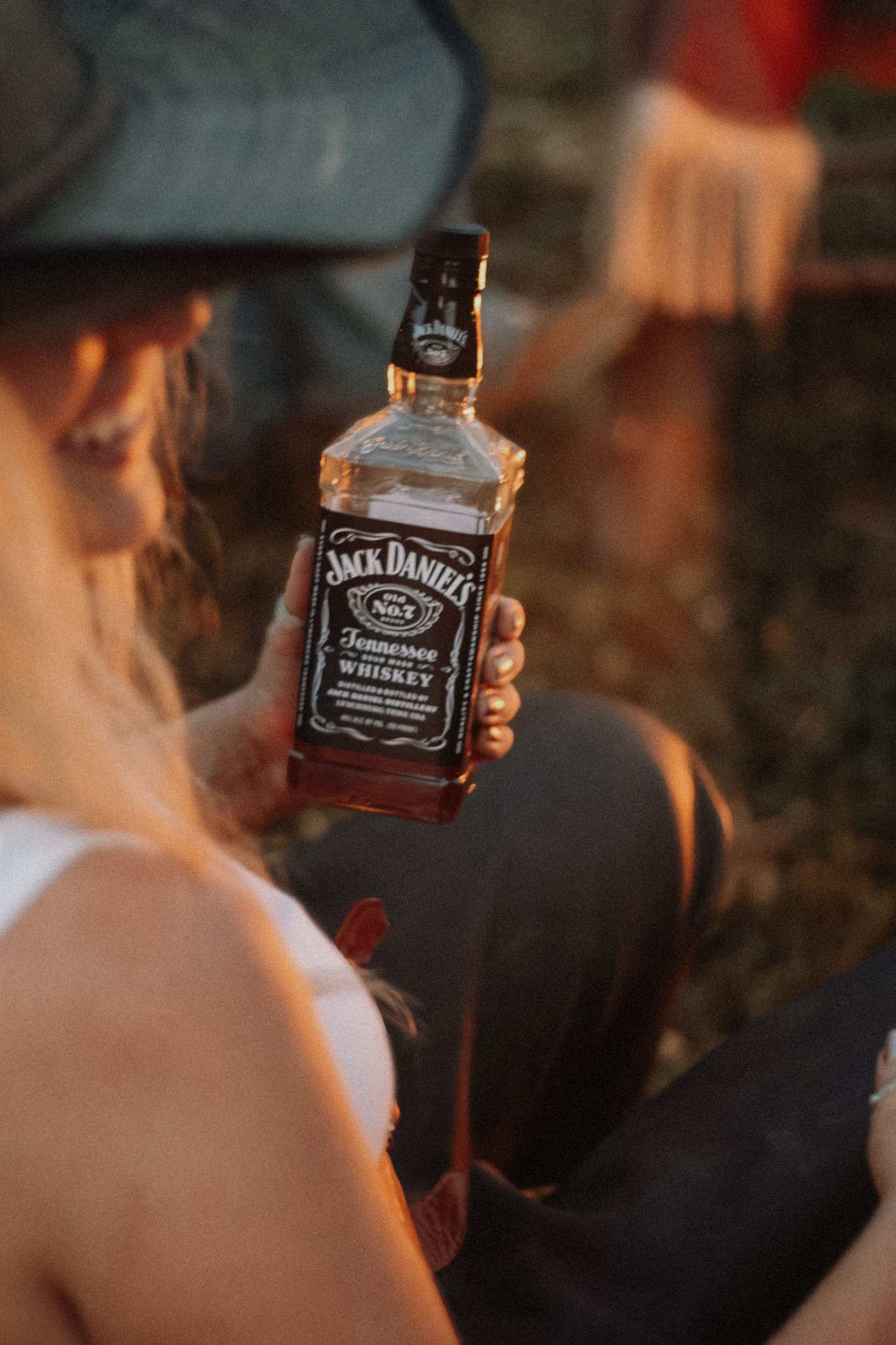 Cowgirl holding up Jack Daniel's bottle at golden hour