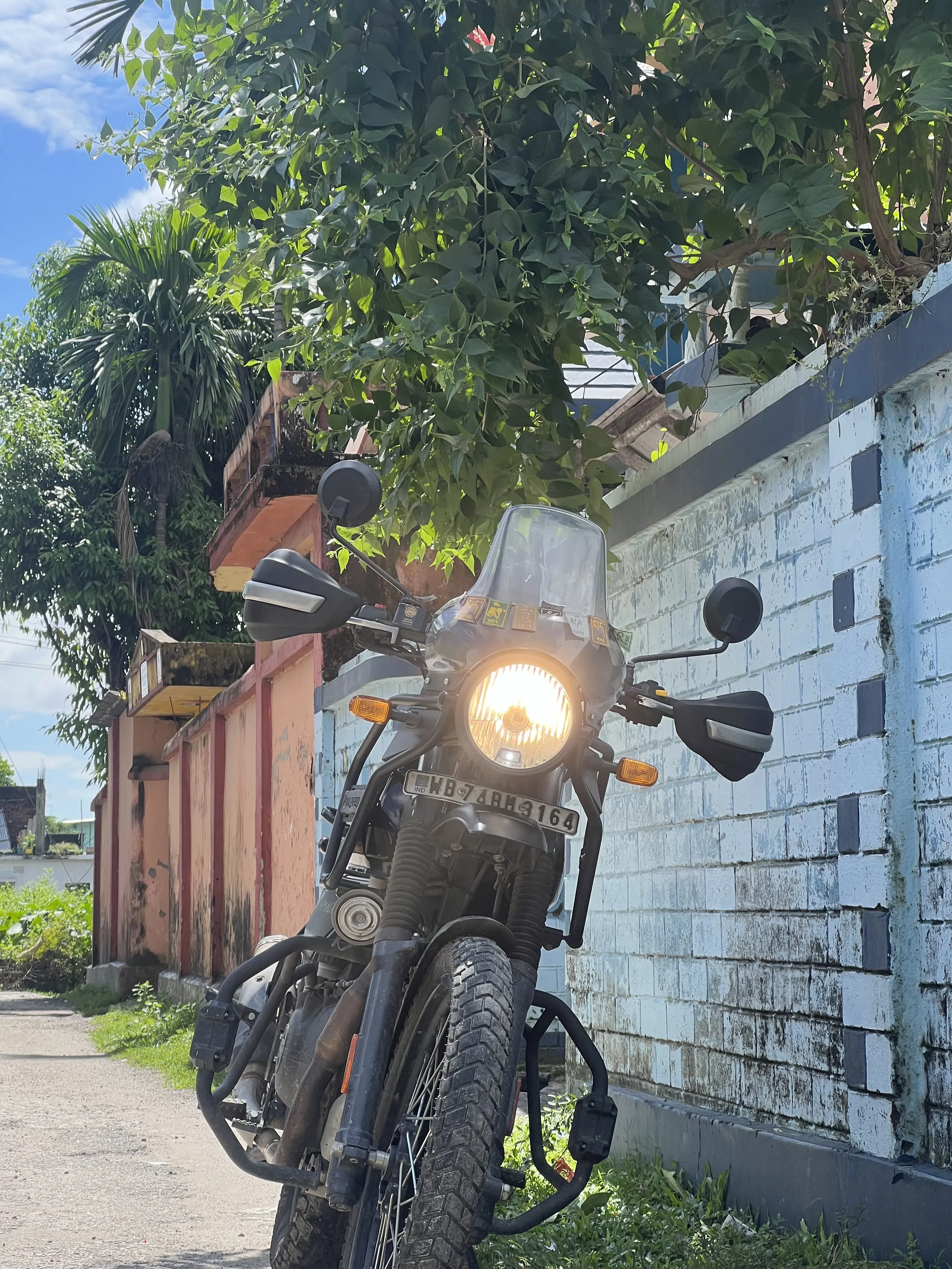 Royal Enfield Himalayan motorcycle with illuminated headlight parked against vintage weathered walls in tropical urban setting, showcasing the authentic street charm of North Bengal motorcycle adventures and local exploration possibilities. Affordable motorcycle rentals in Bagdogra for exploring North Bengal.