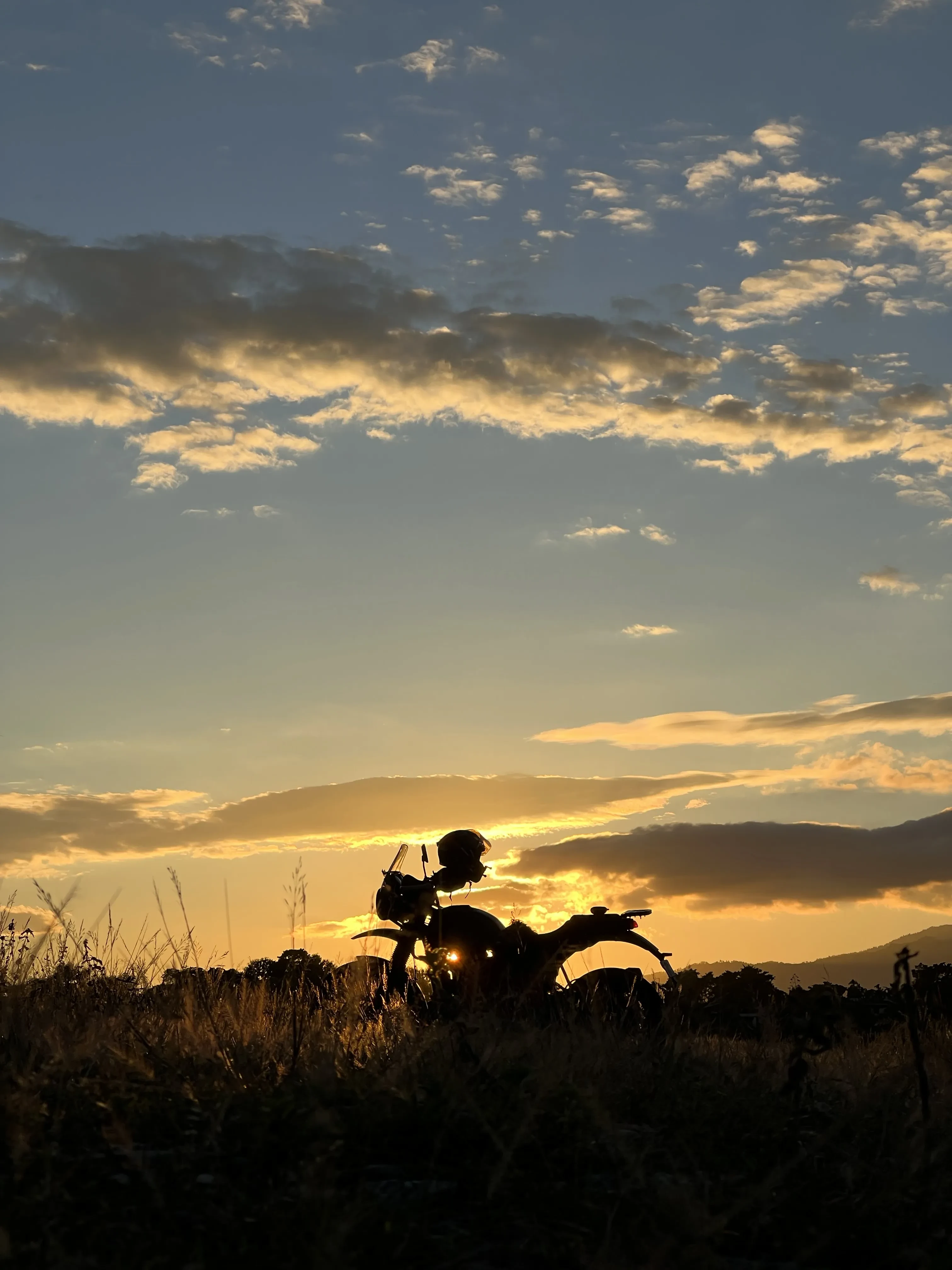 Silhouette of a Royal Enfield motorcycle against a dramatic Himalayan sunset, showcasing adventure touring in the mountains with golden clouds and mountain peaks in the background. Affordable motorcycle rentals in Darjeeling for sunset rides.