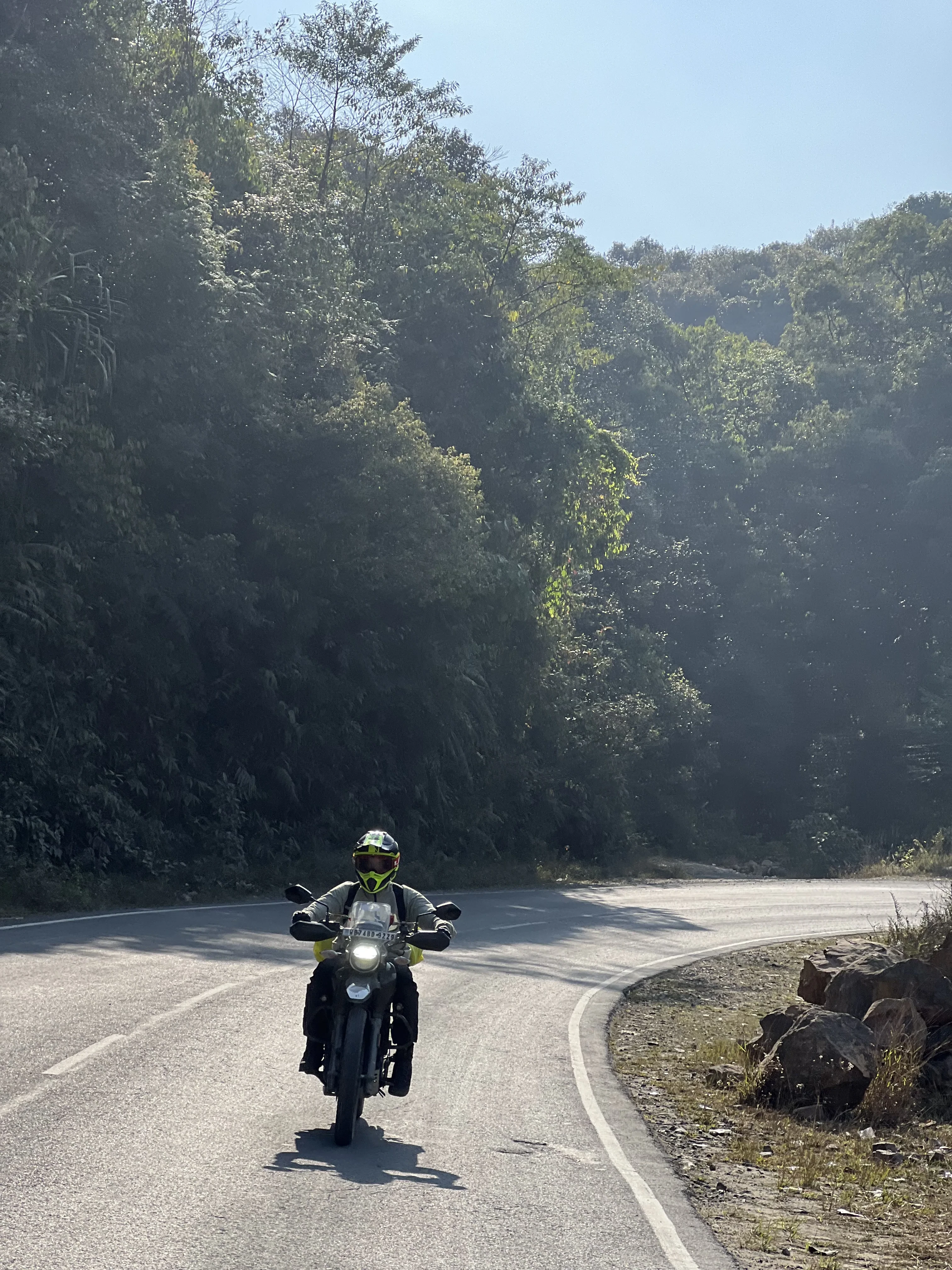 Motorcyclist navigating a scenic mountain curve on a Hero XPulse 200 2V, surrounded by lush Himalayan forest and perfect riding conditions on a well-maintained road. Affordable motorcycle rentals in Sikkim for mountain road adventures.