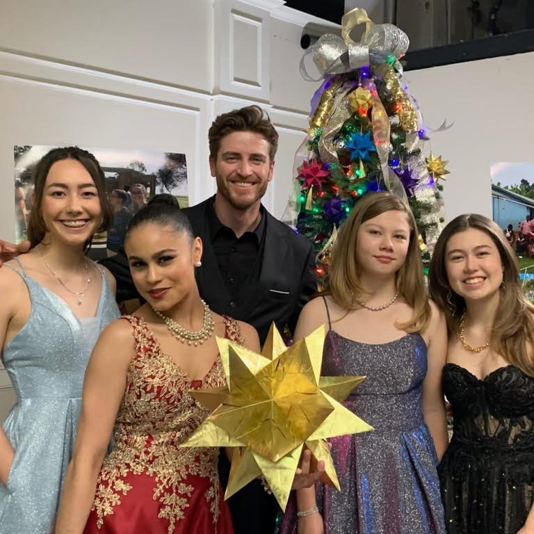 Paper for Water volunteers Isabelle, Katherine, and Trinity on the Gingersnap Christmas set holding a large gold origami star with cast members