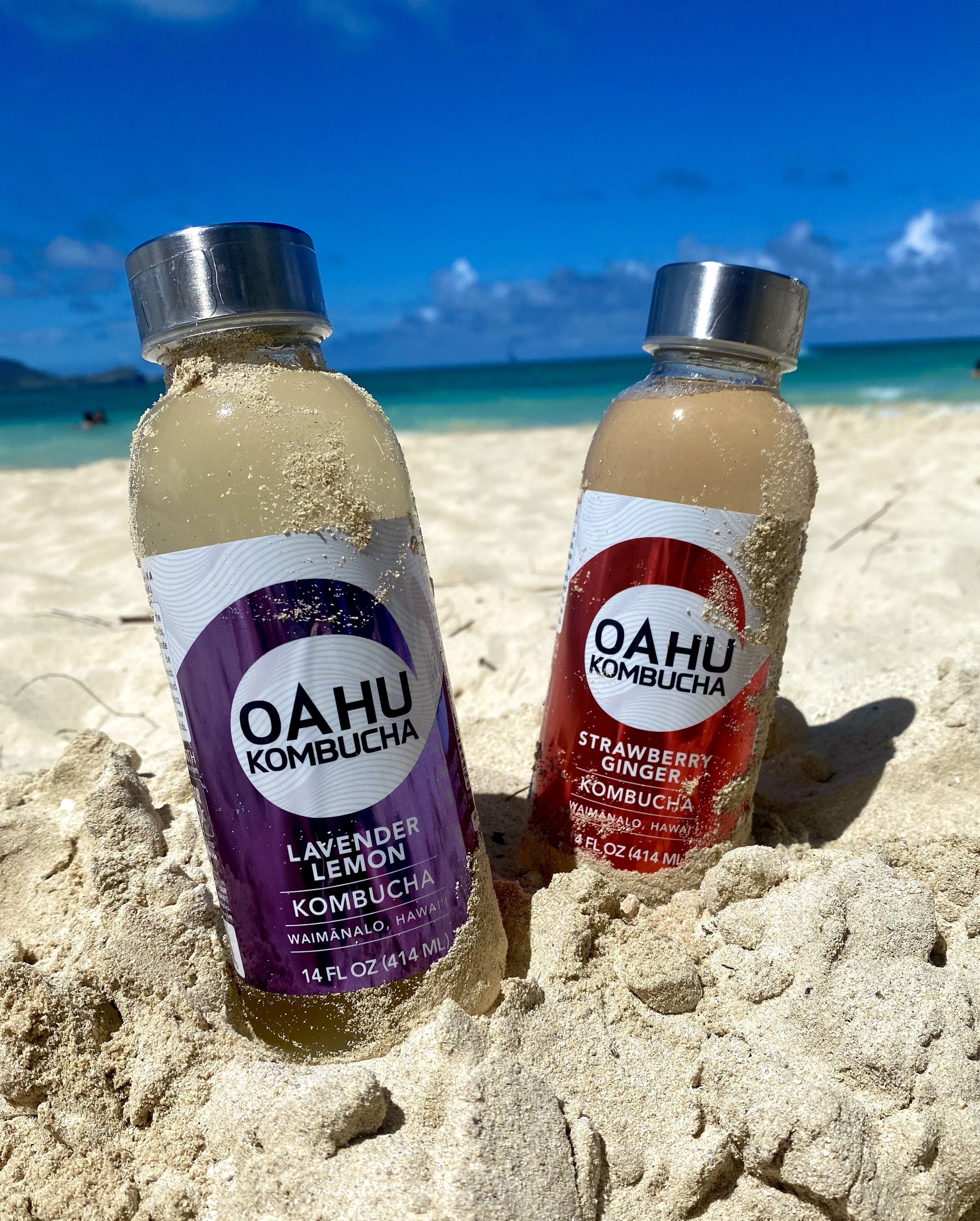 Lavender Lemon and Strawberry Ginger bottles in beach sand